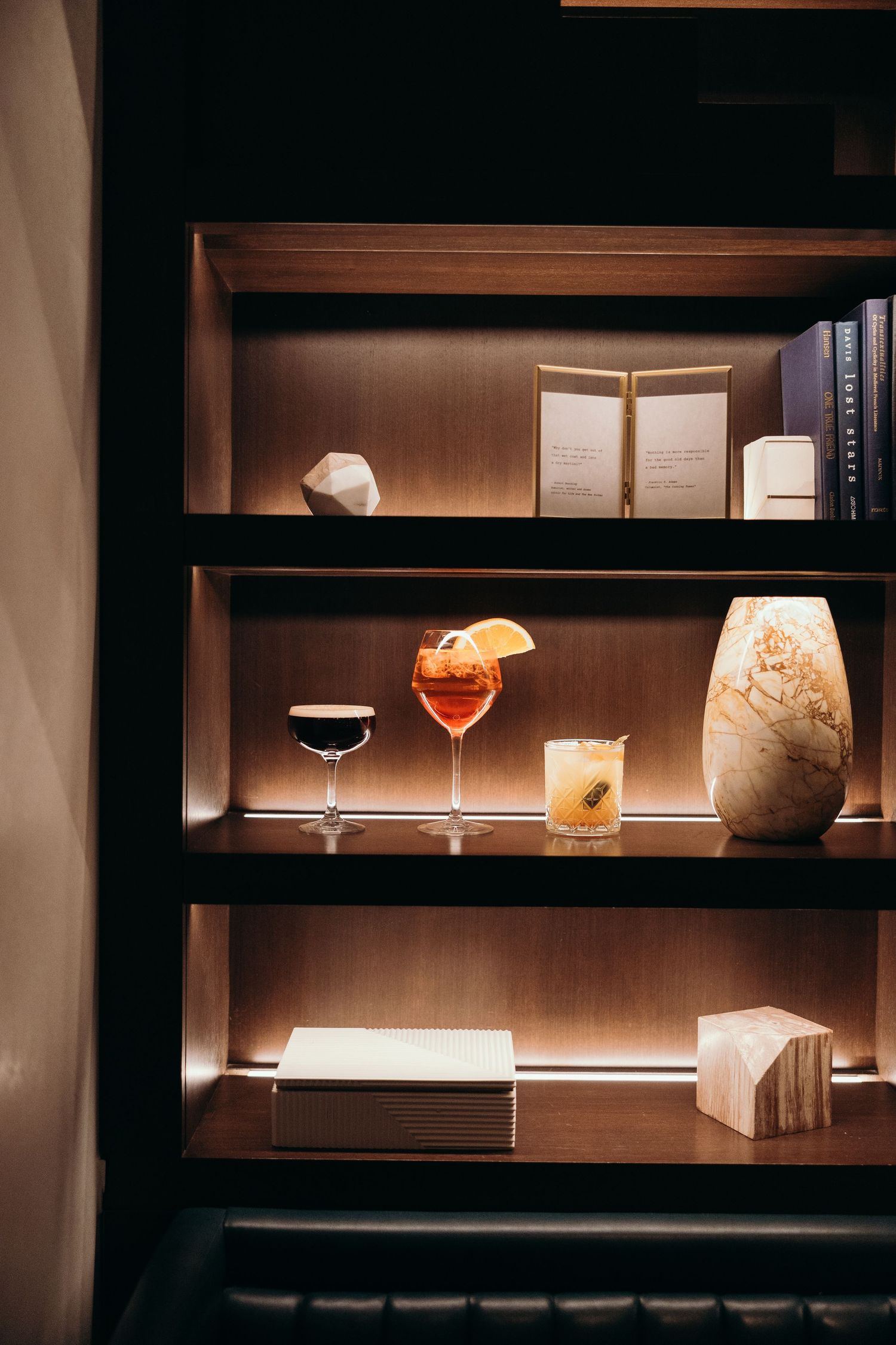 Illuminated shelving displays elegant cocktail glasses and decorative objects in a modern bar setting.