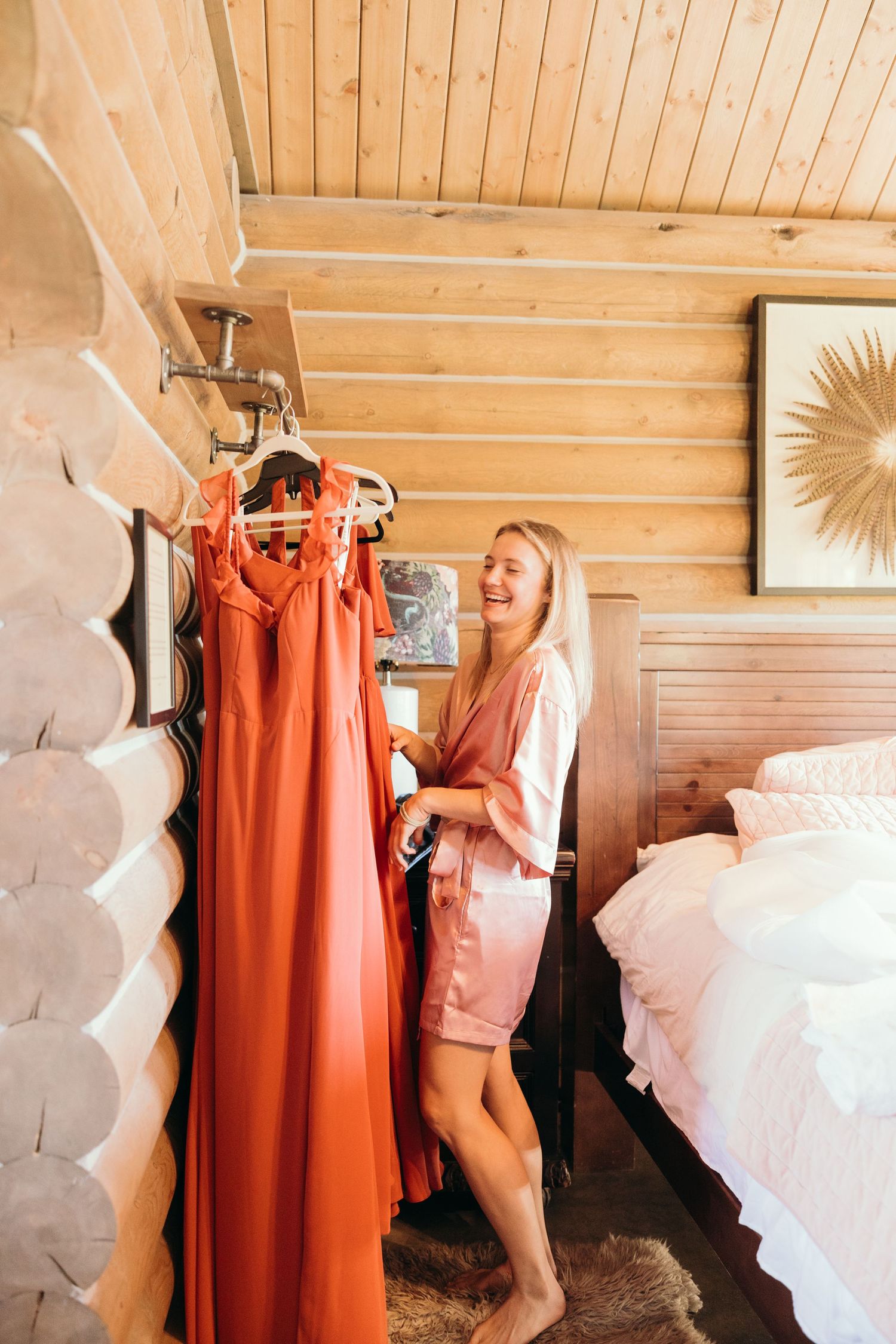 Wedding preparation scene with orange bridesmaid dress hanging in rustic log cabin room.