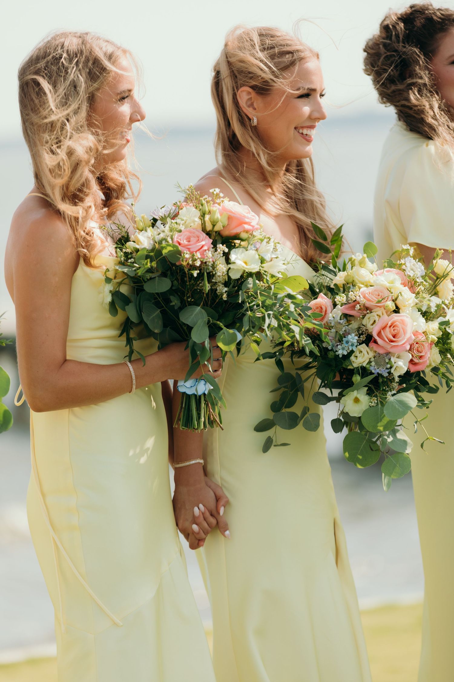 Bridesmaids in pale yellow dresses hold lush floral bouquets while standing in a row.
