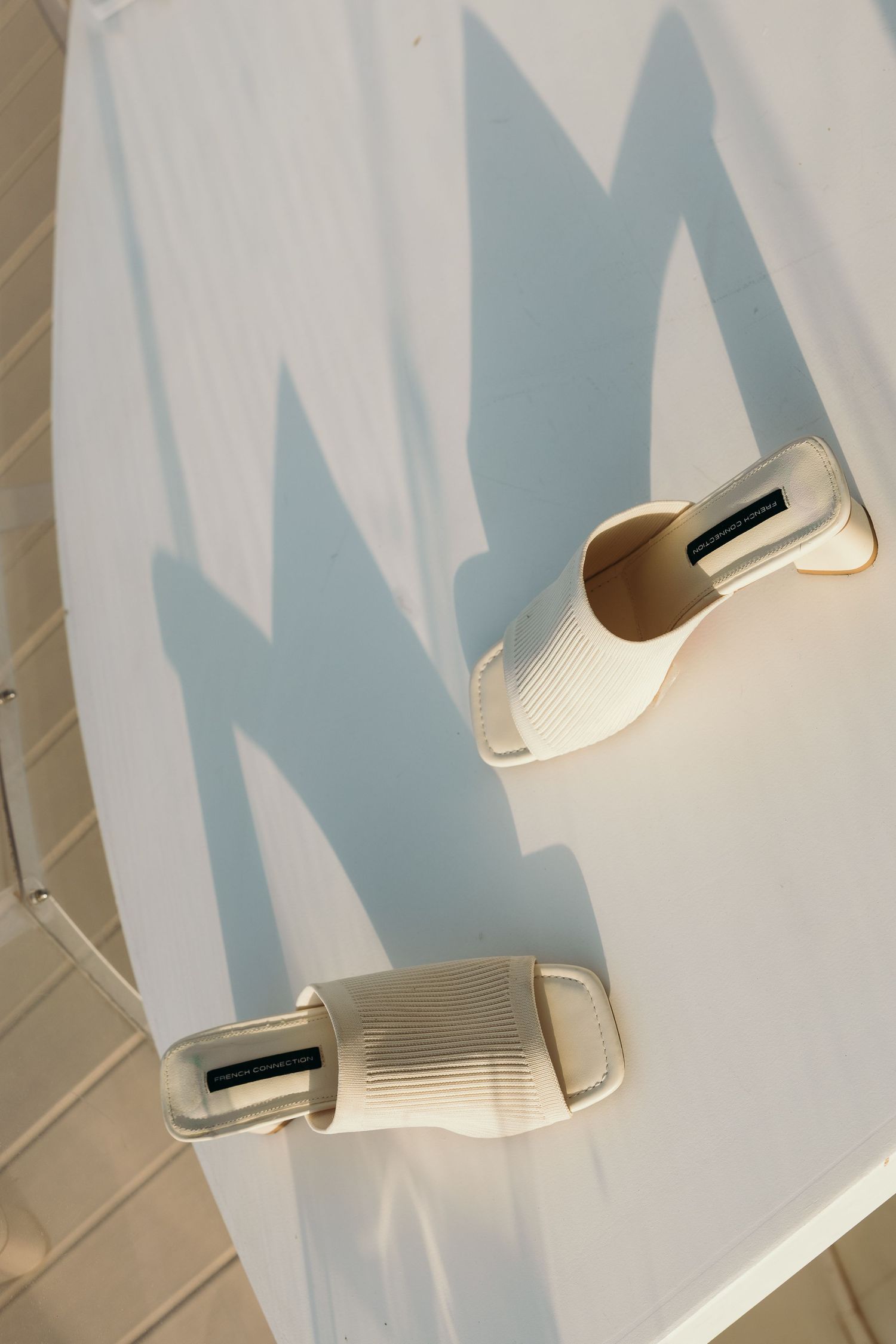 White bridal shoes casting shadows on a light wall background.