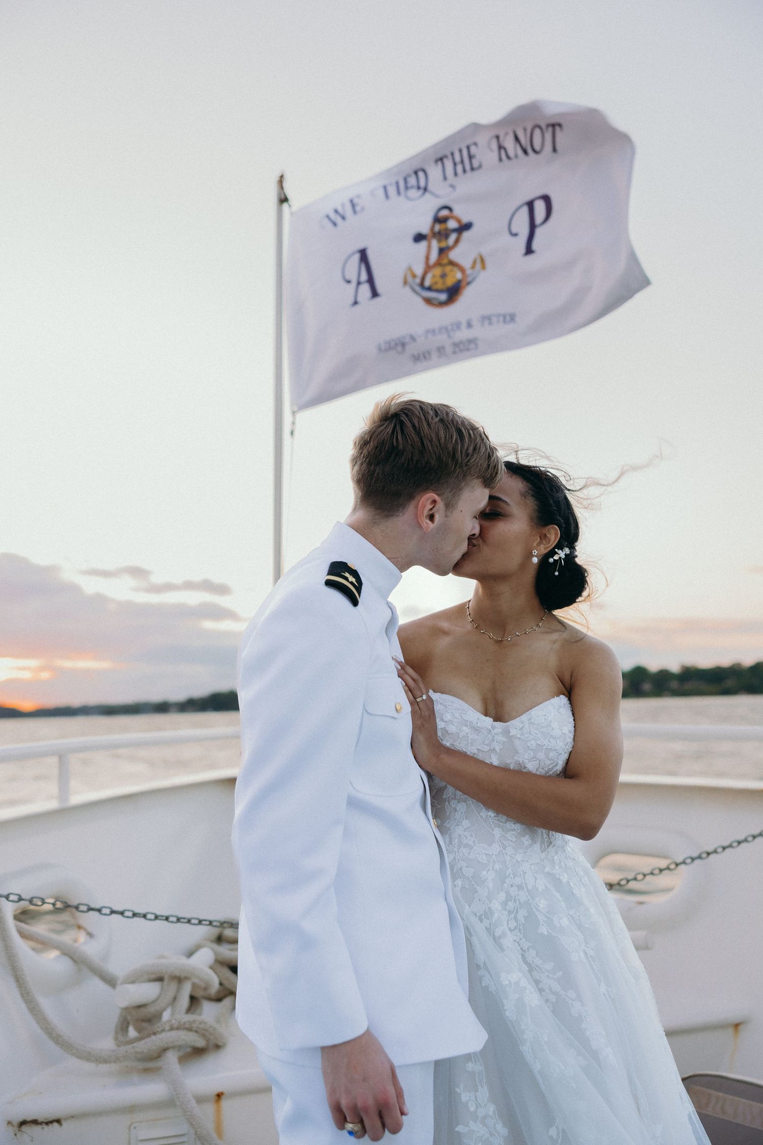 A romantic moment between newlyweds on a boat deck with flags waving in the background.
