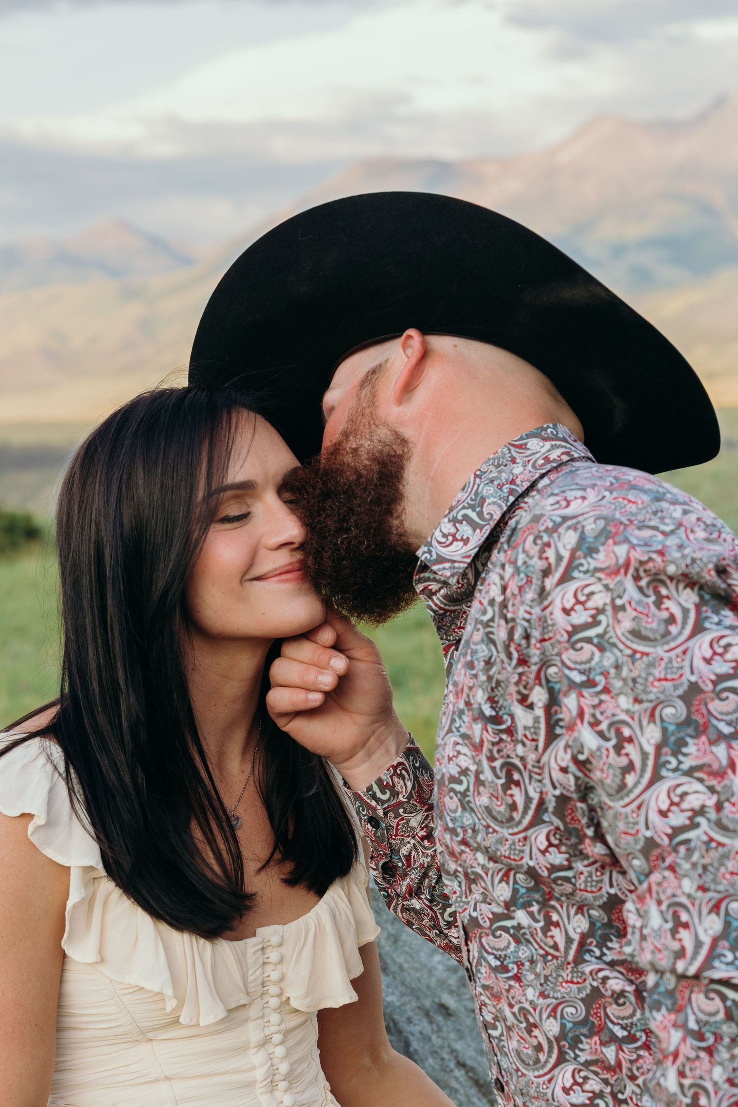 Romantic couple sharing tender moments against a mountain backdrop at sunset.