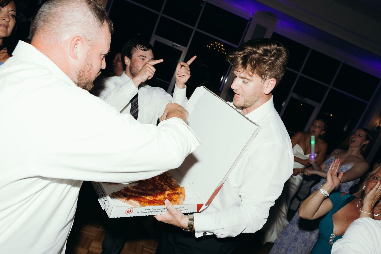 Wedding guests dancing and mingling on a dark dance floor with purple lighting.