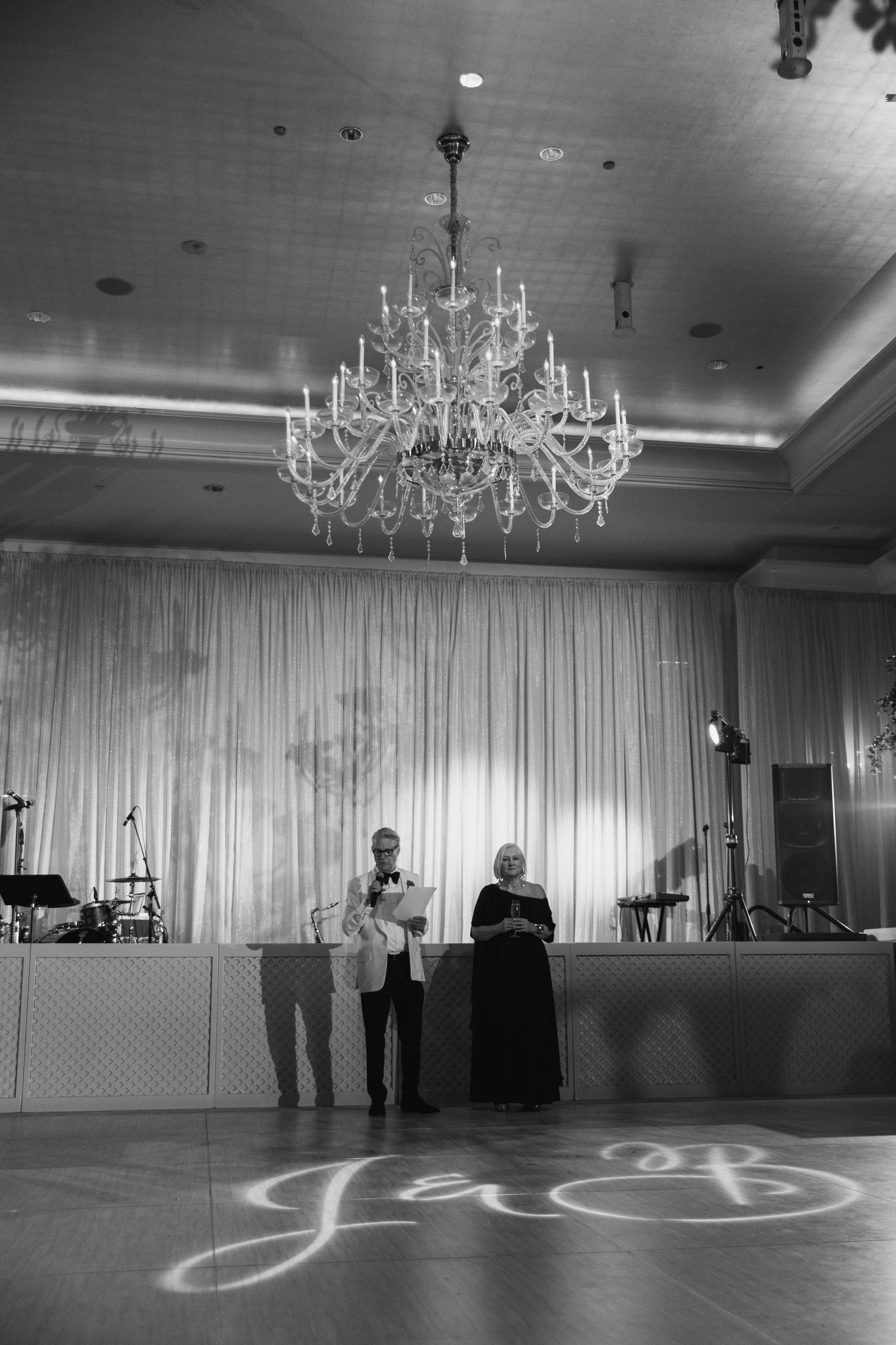 An elegant ballroom with crystal chandeliers and a light pattern projected on the dark floor.