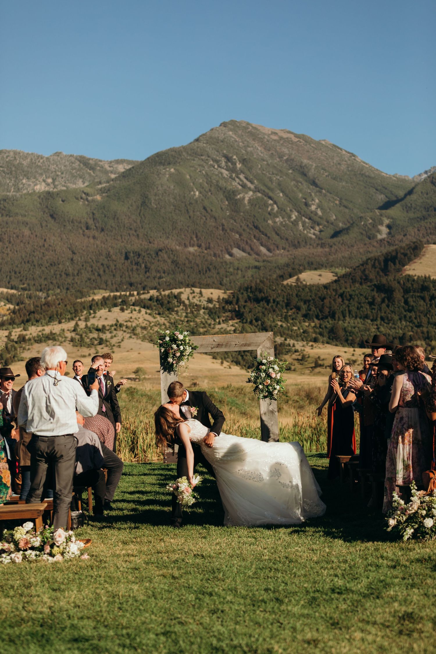 Wedding celebration in a grassy field with dramatic mountain backdrop.