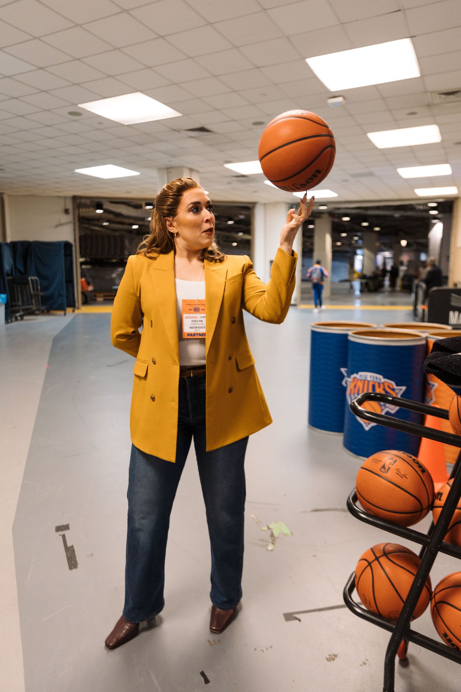 Jessica Vosk in yellow blazer plays with basketballs in indoor space.