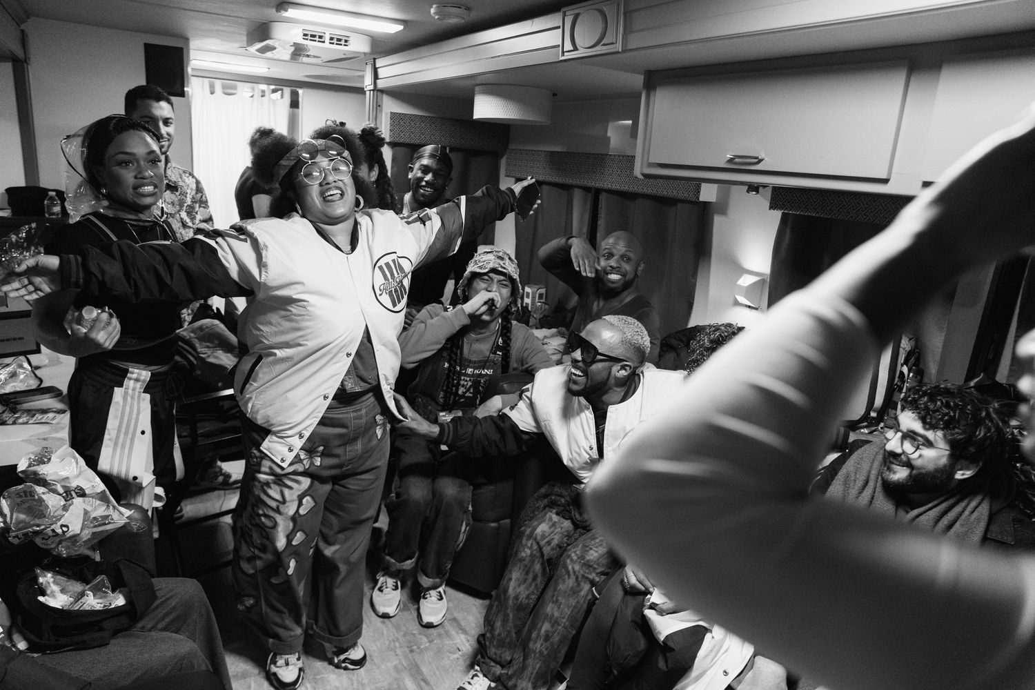 A crowded backstage scene shows energetic performers celebrating in black and white.