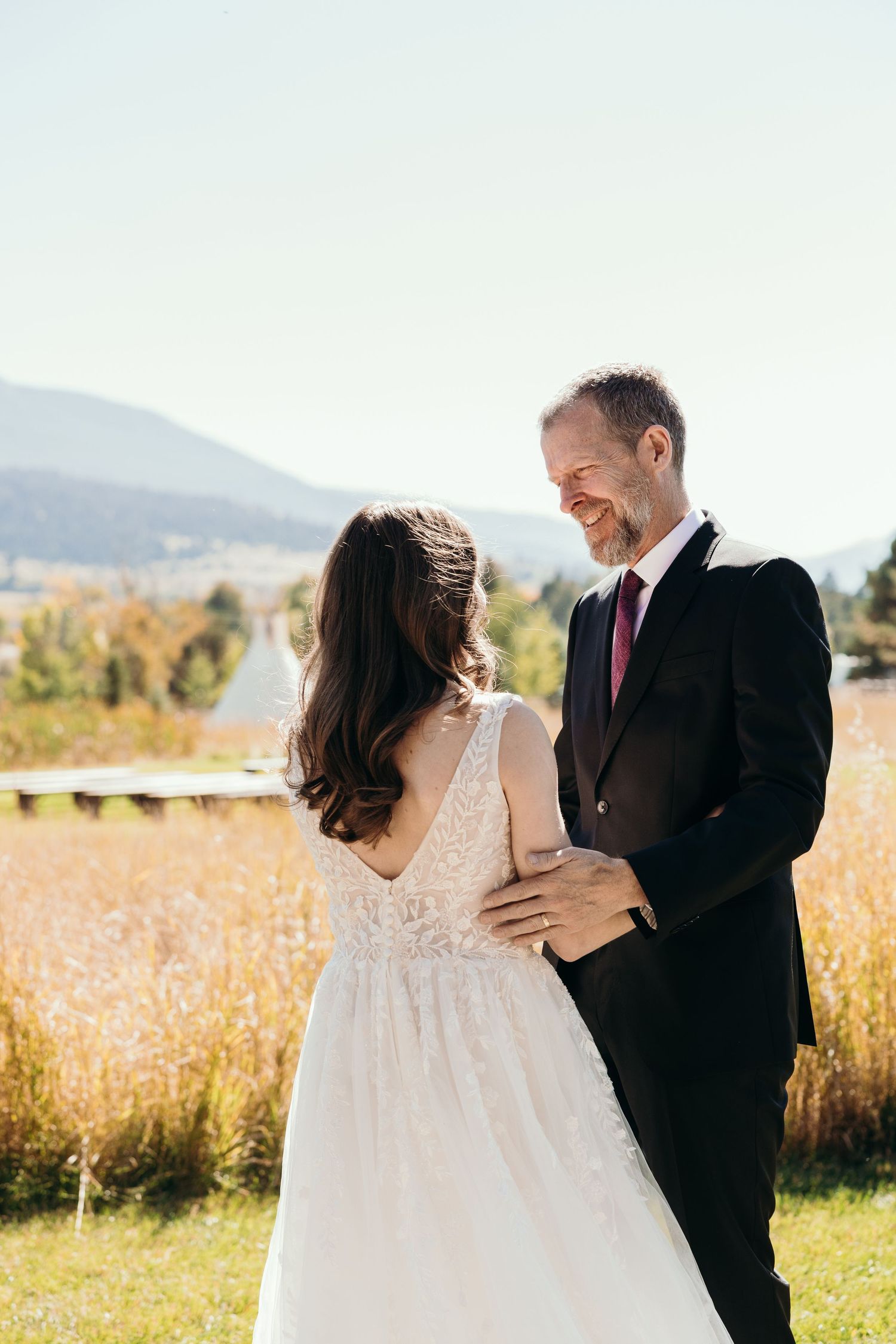 Romantic wedding portrait of couple embracing in sunlit mountain meadow.