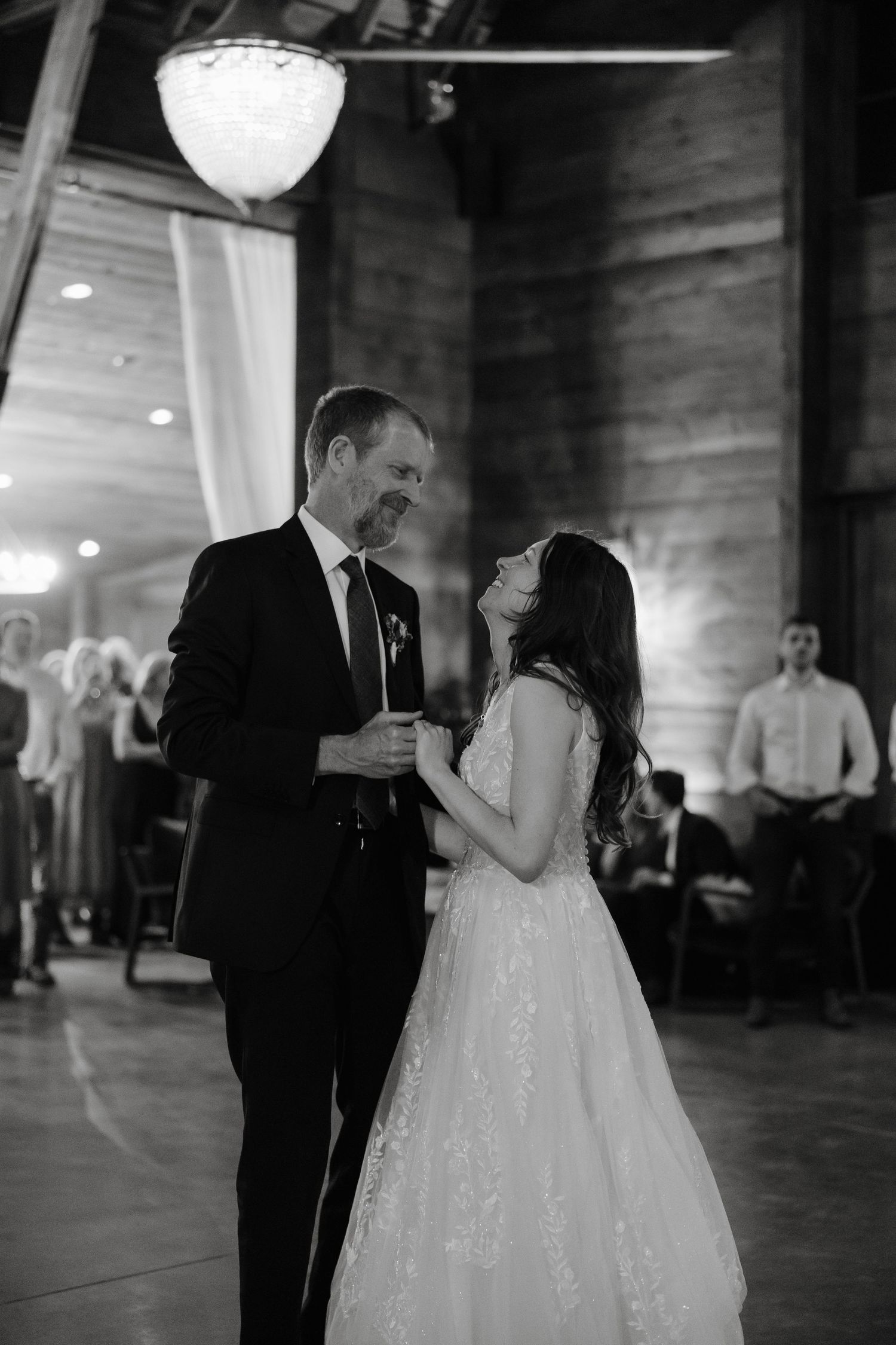 A couple shares their first dance under paper lanterns in a rustic wooden venue.