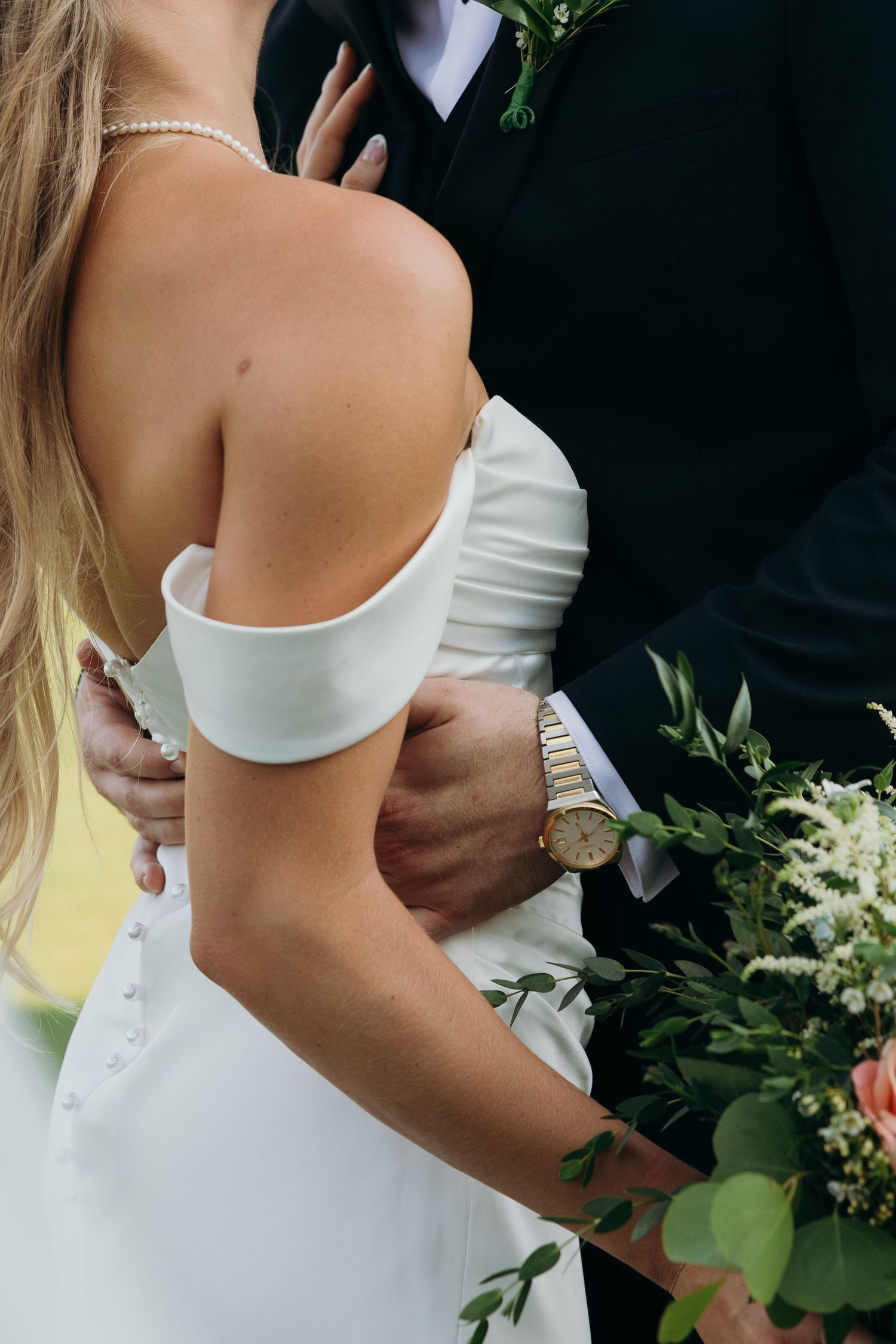 Close-up details of an off-shoulder white wedding dress with pearl accessories.