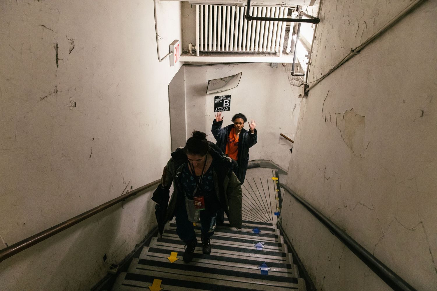 People descend a dimly lit concrete stairwell in an urban setting.