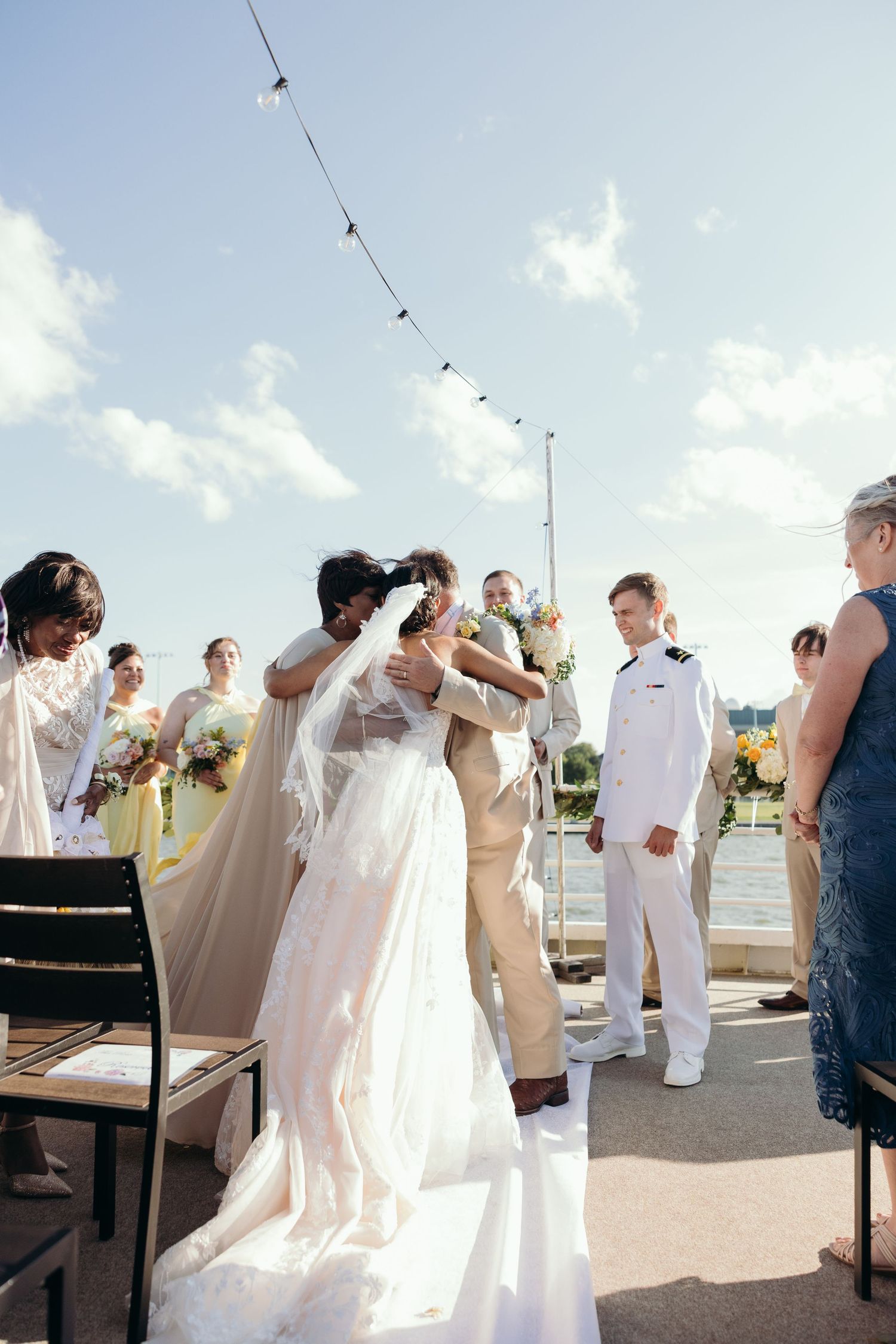 Wedding party members in white and beige attire mingle during an outdoor celebration.