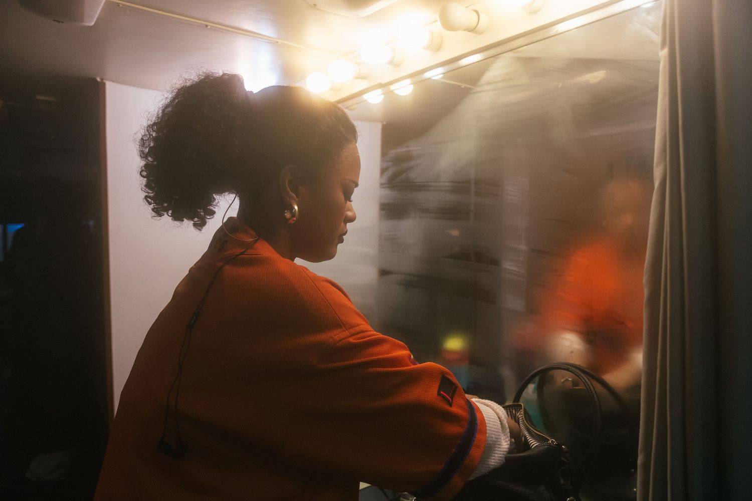 A person in an orange jacket sits silently by a window during a nighttime journey.