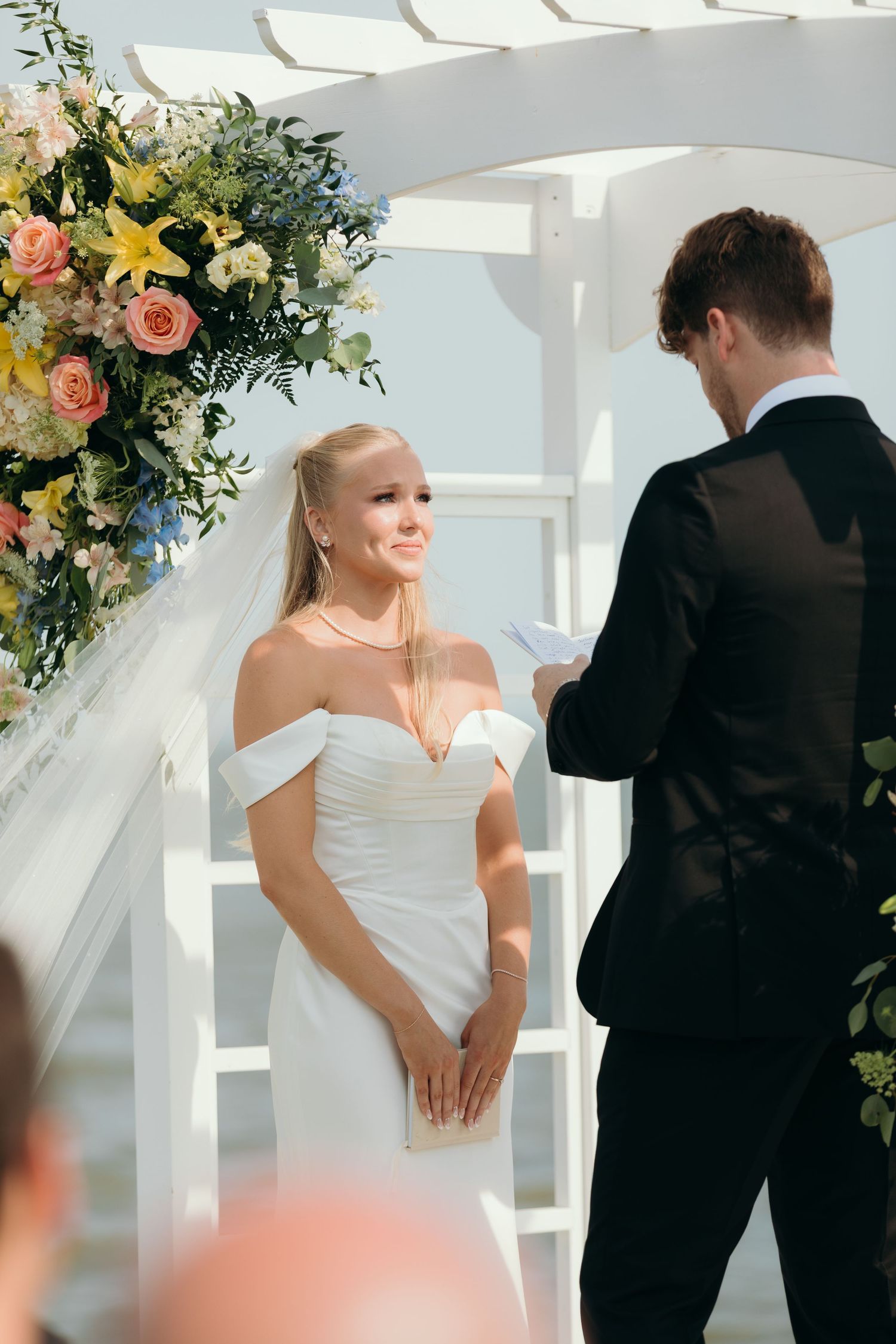 Intimate wedding ceremony moments under a white pergola decorated with colorful floral arrangements.