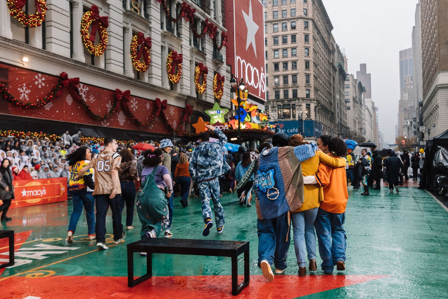A crowd gathers on a green street surface in New York City with tall buildings and holiday decorations visible.