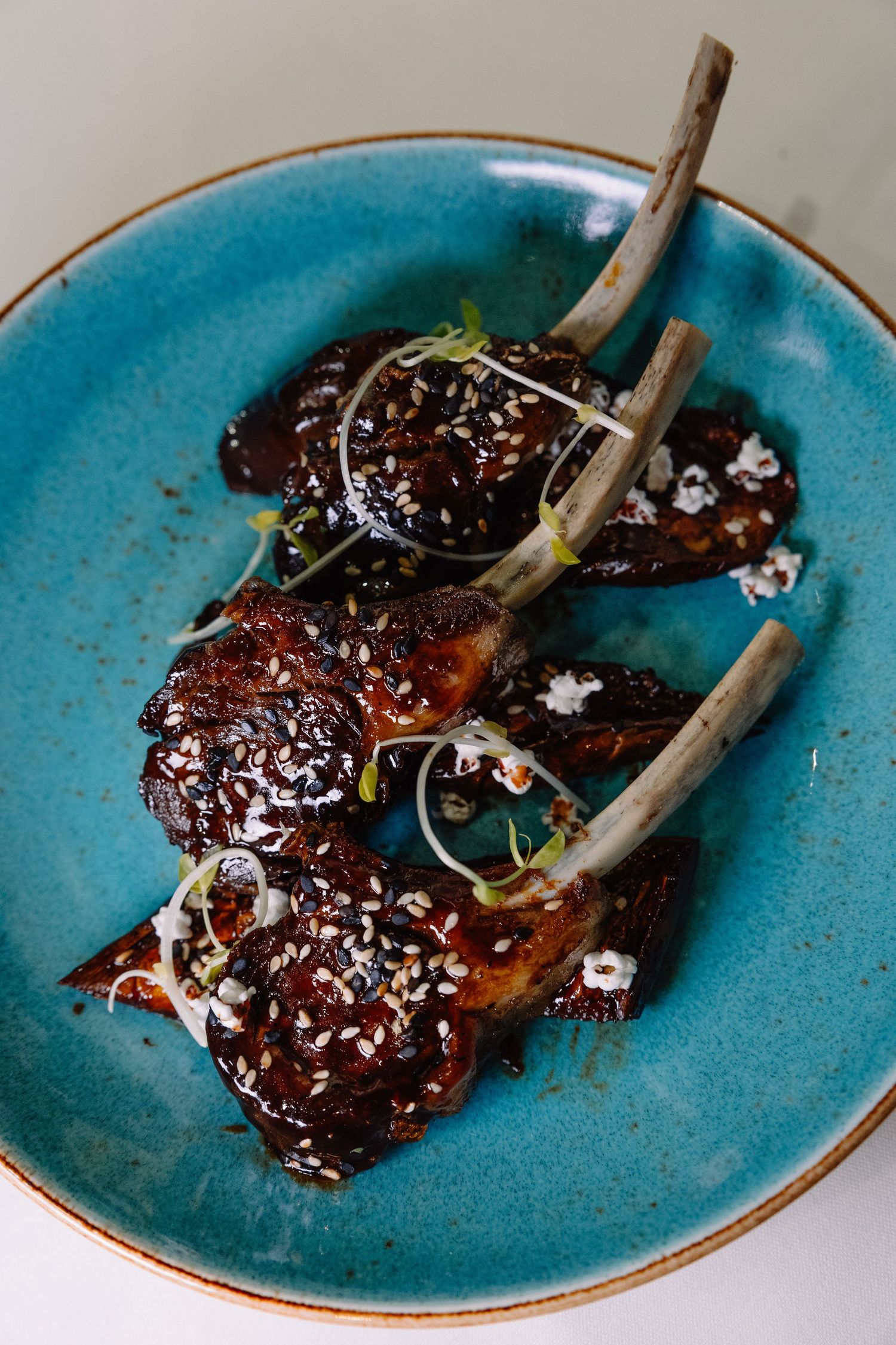 Glazed beef short ribs with garnish served on turquoise ceramic plates in a progression of plating steps.