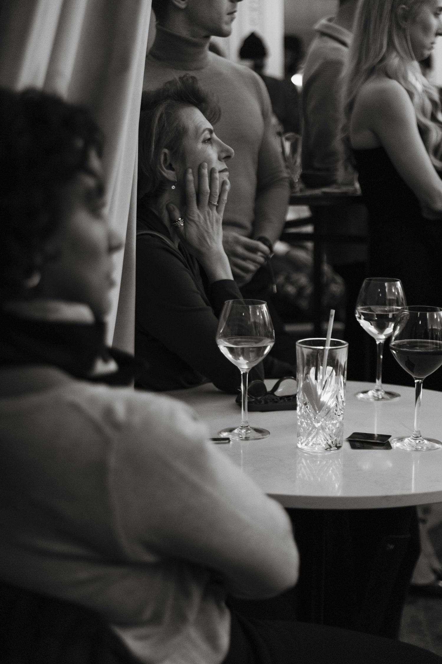 A series of black and white photos showing wine glasses and people sitting at a bar in dim lighting.