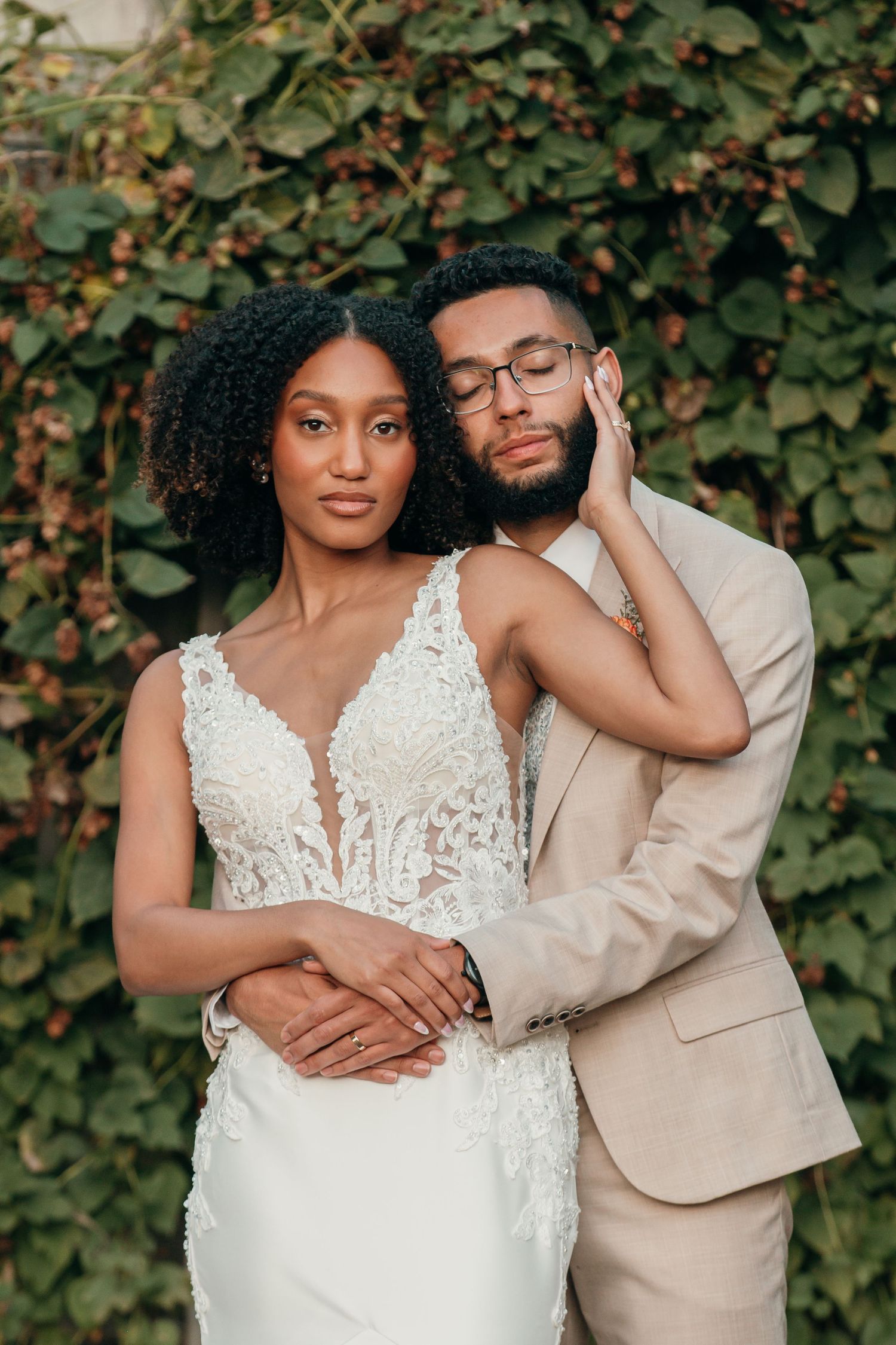Romantic wedding portrait of couple embracing against lush green foliage backdrop.