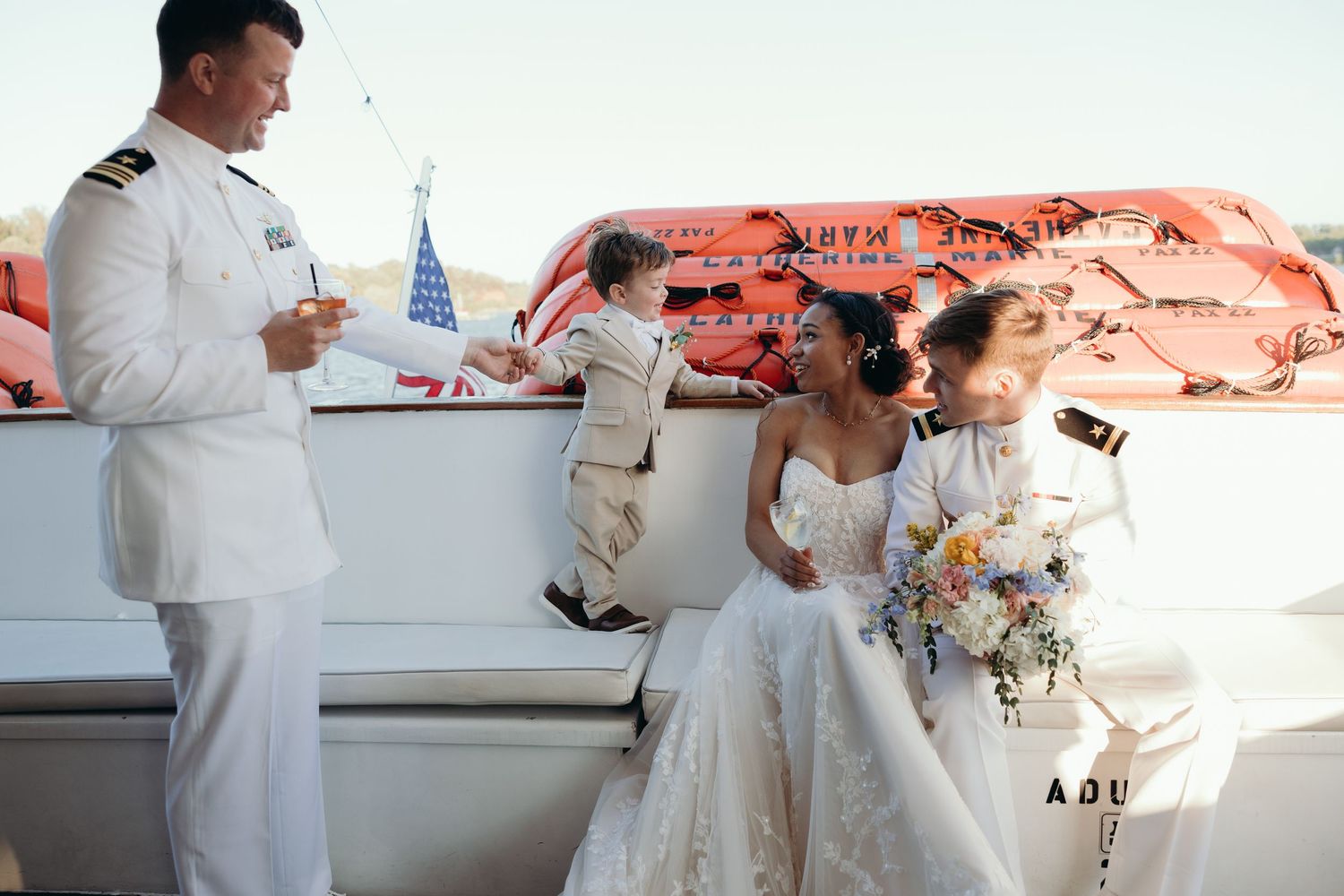 Wedding party members in white attire celebrate with champagne on an outdoor deck.