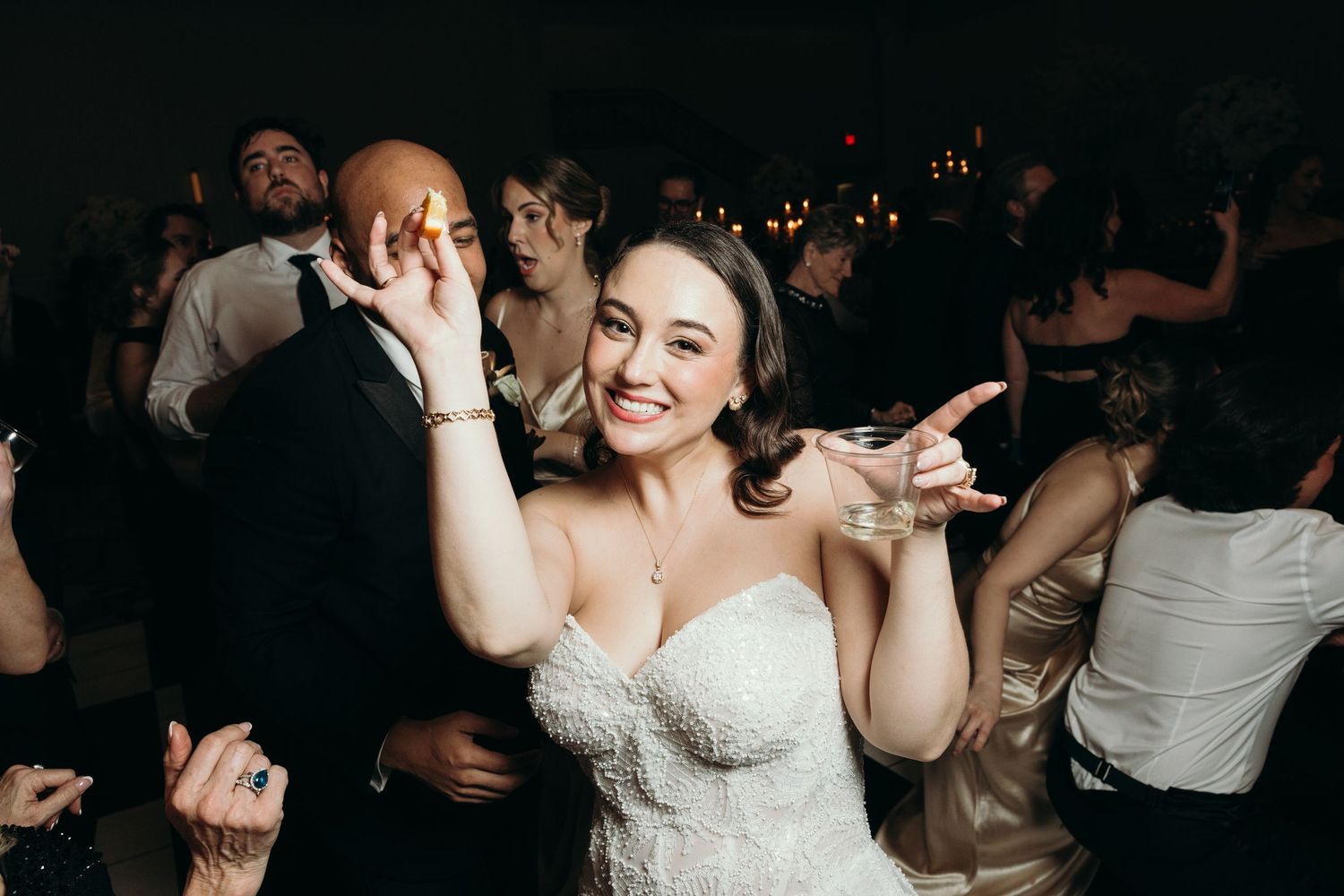 A couple dances together at a wedding reception surrounded by other guests on a dark dance floor.