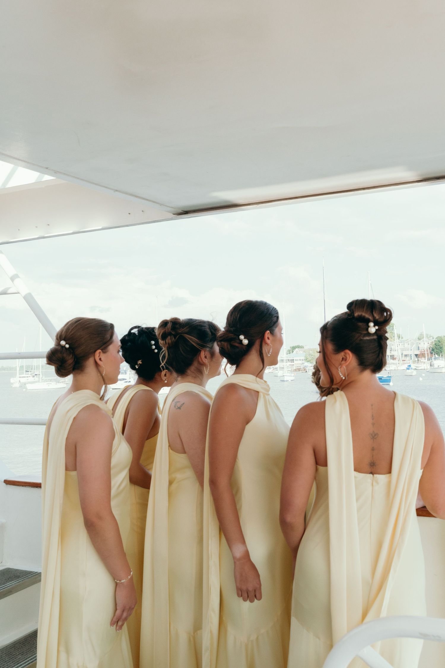 Row of bridesmaids in pale yellow dresses standing on a boat deck.
