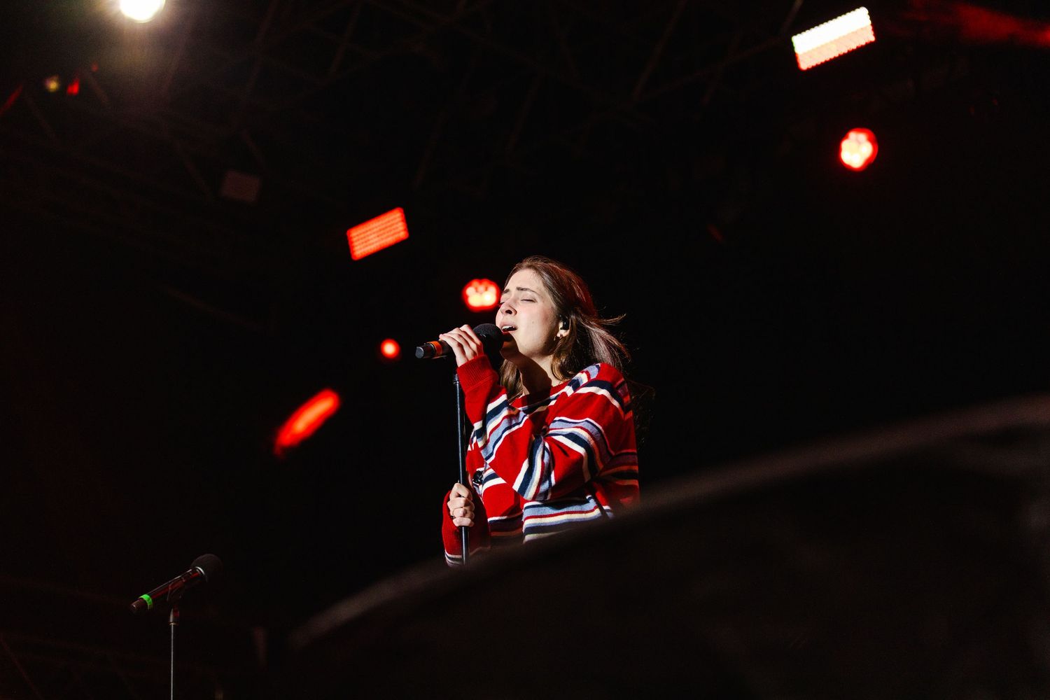 Lizzie McAlpine singing on stage with dramatic spotlight illumination.