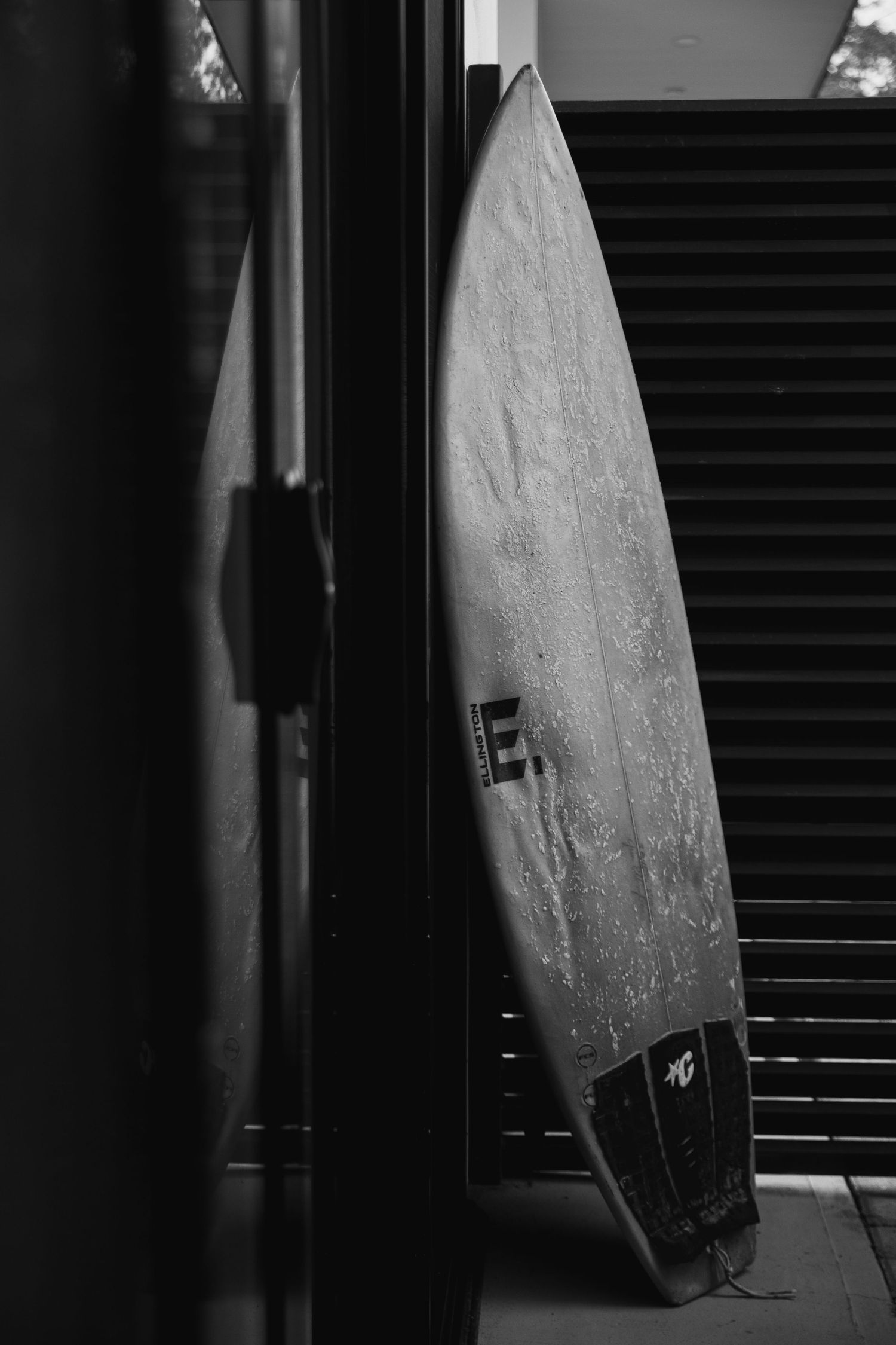 Surfboard leans against dark wall with dramatic shadows and lighting.