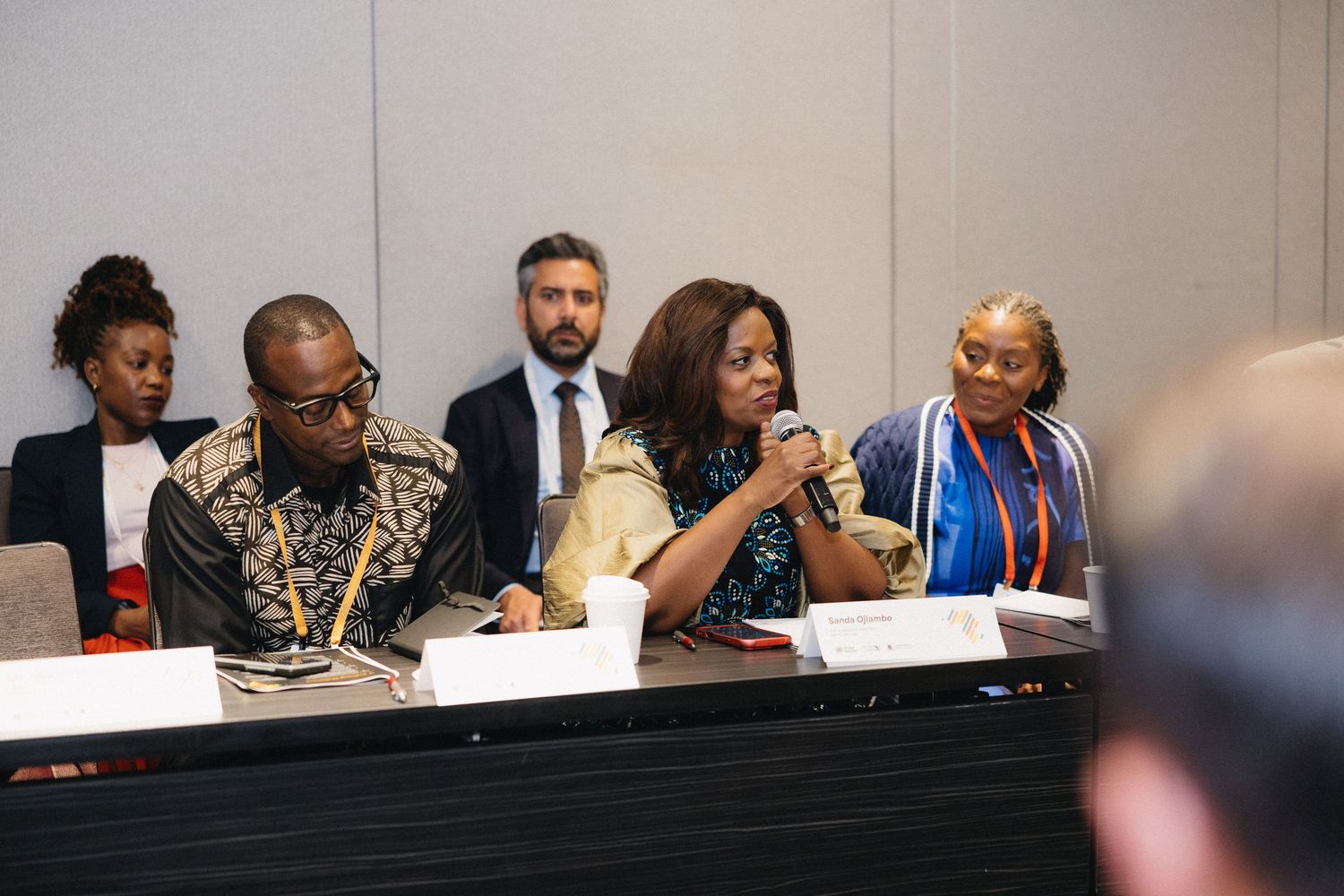 Business professionals sit at a long conference table during a meeting or presentation.