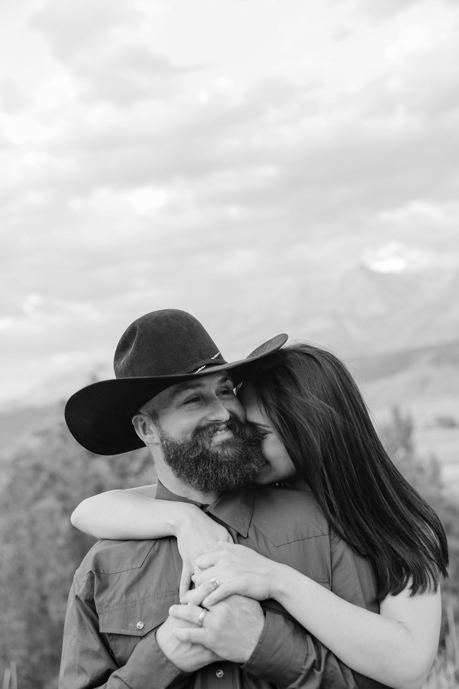 A black and white photo captures an intimate moment between a couple outdoors.