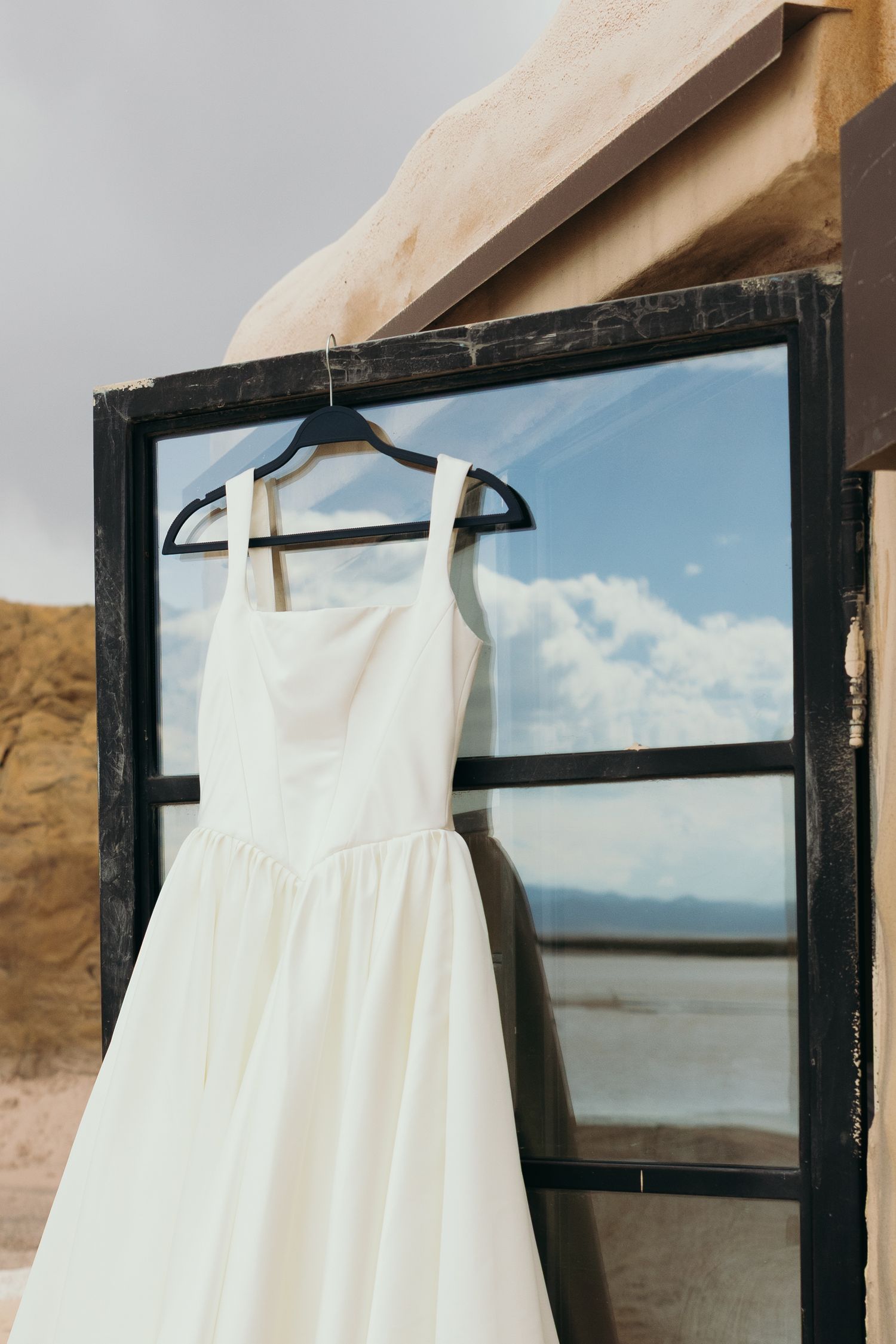 White wedding dress hanging in window frame with desert landscape view.