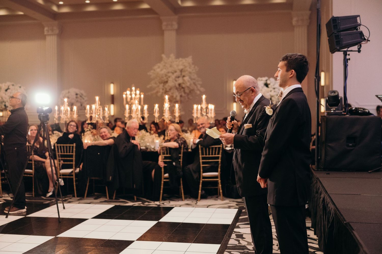 A series of black and white checkered dance floors at an elegant ballroom event with guests mingling in formal attire.