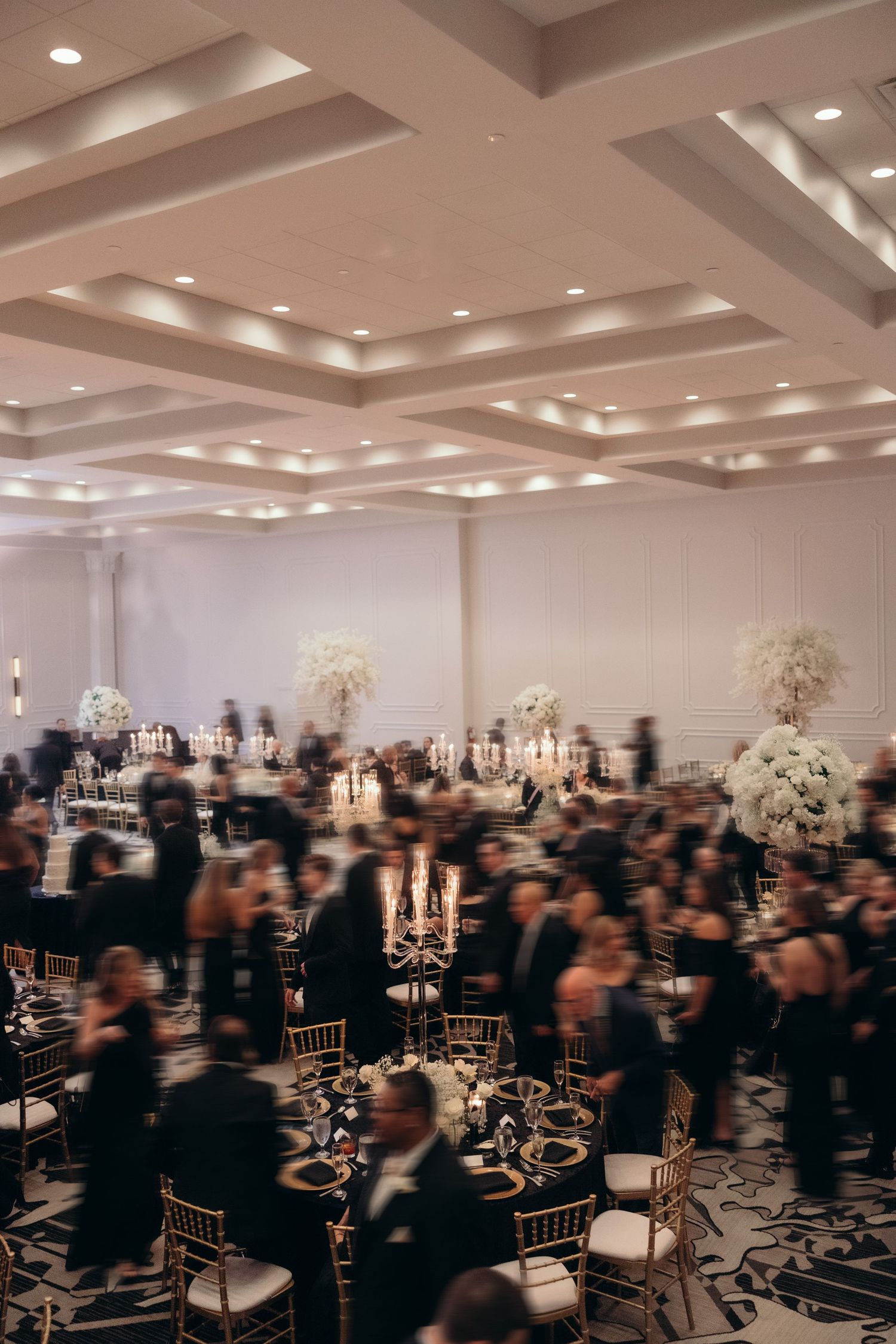 A panoramic view of an elegant wedding reception venue with gold chairs and white floral arrangements.