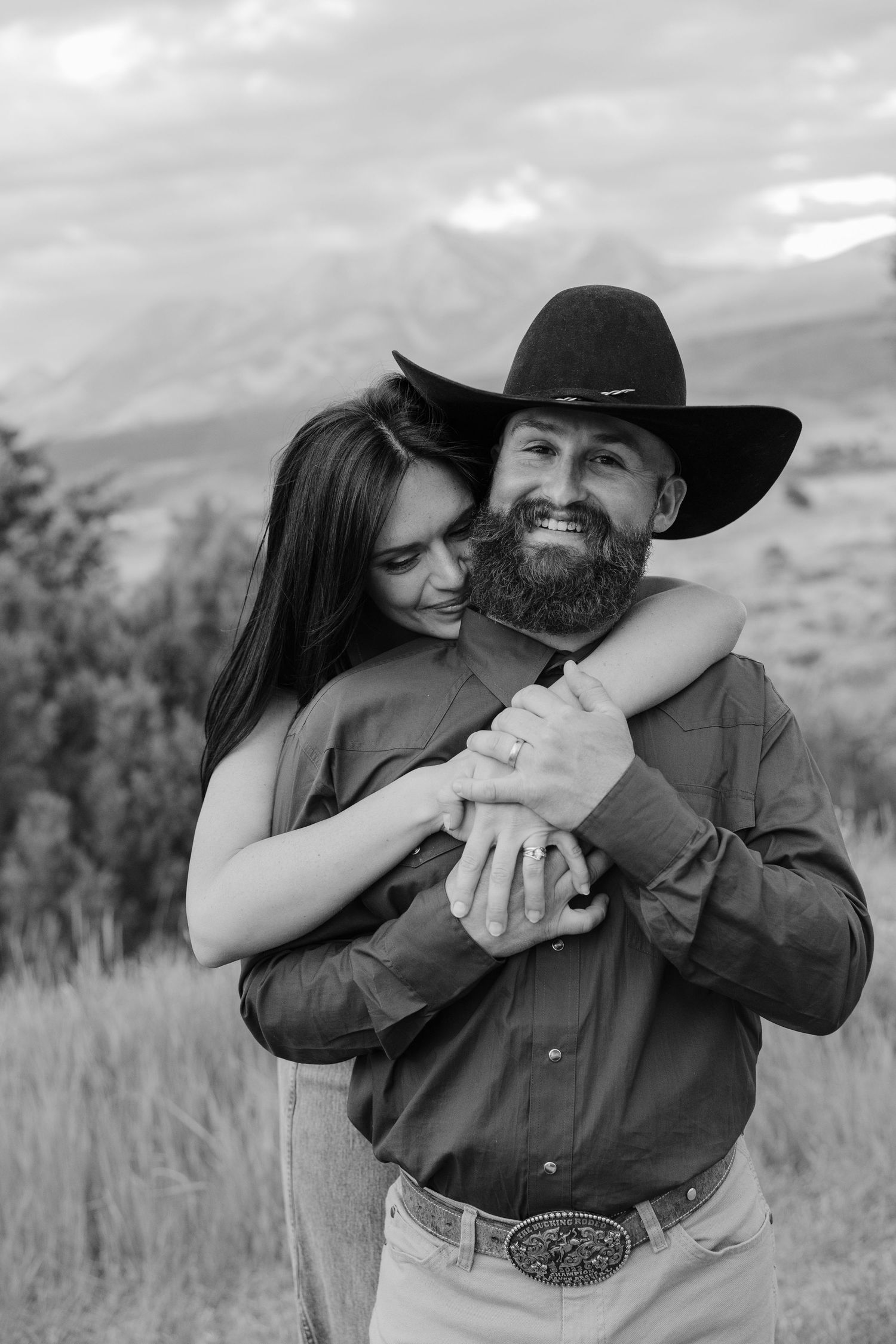 A black and white photo shows a couple in western attire sharing a tender embrace.