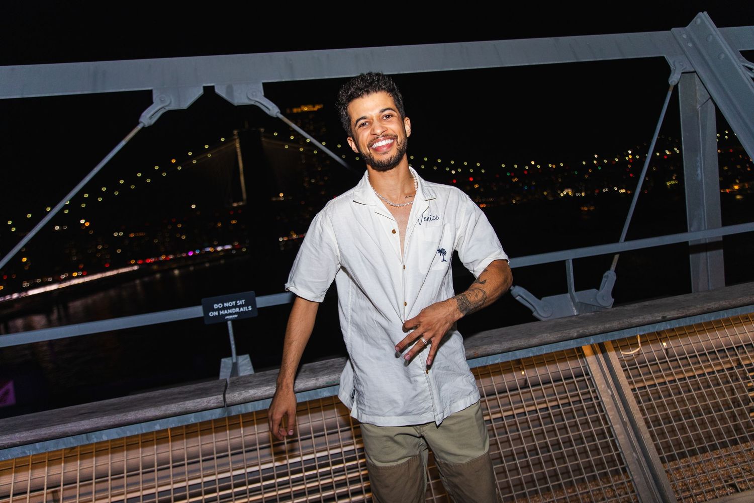 Jordan Fisher at Elise Fest, rooftop venue at night with city lights in background.
