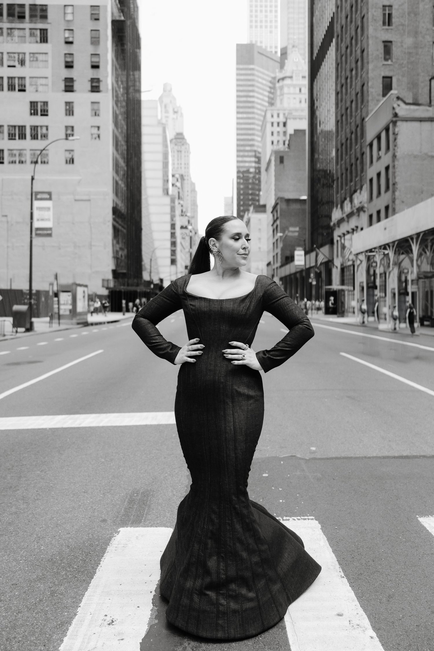 A dramatic black and white photo of someone in a fitted black evening gown posing in the middle of a New York City street.