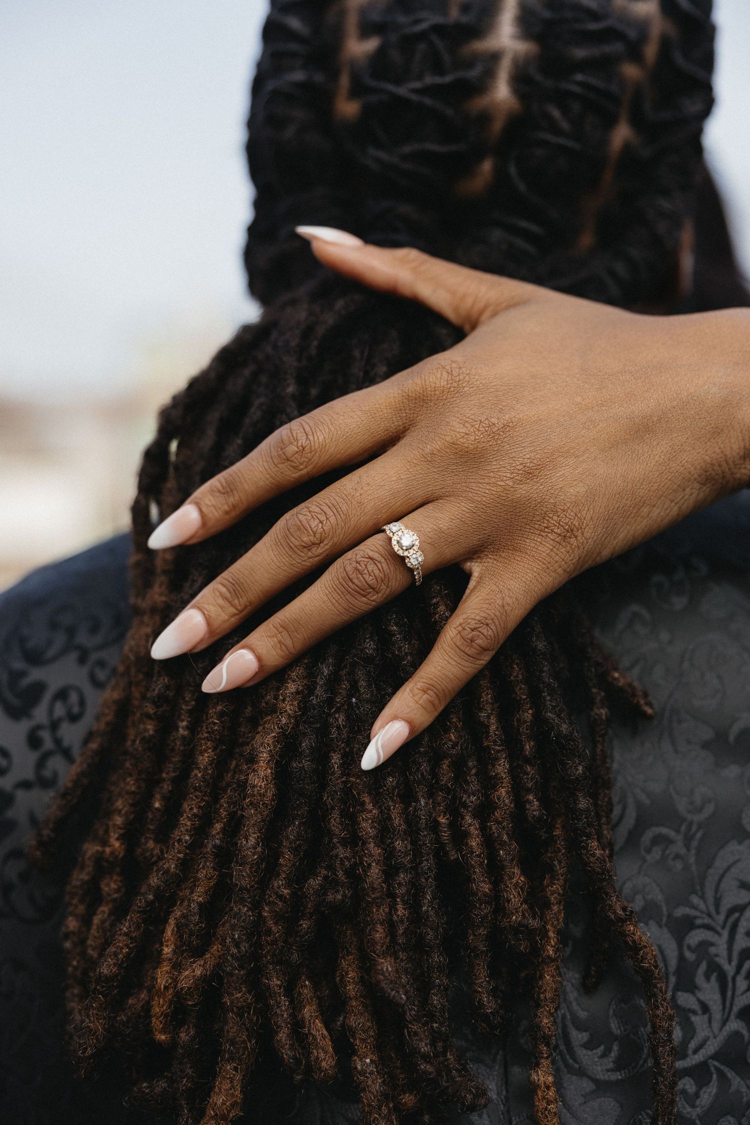 Close-up of a hand with white nails gently touching dreadlocks against a black textured fabric.