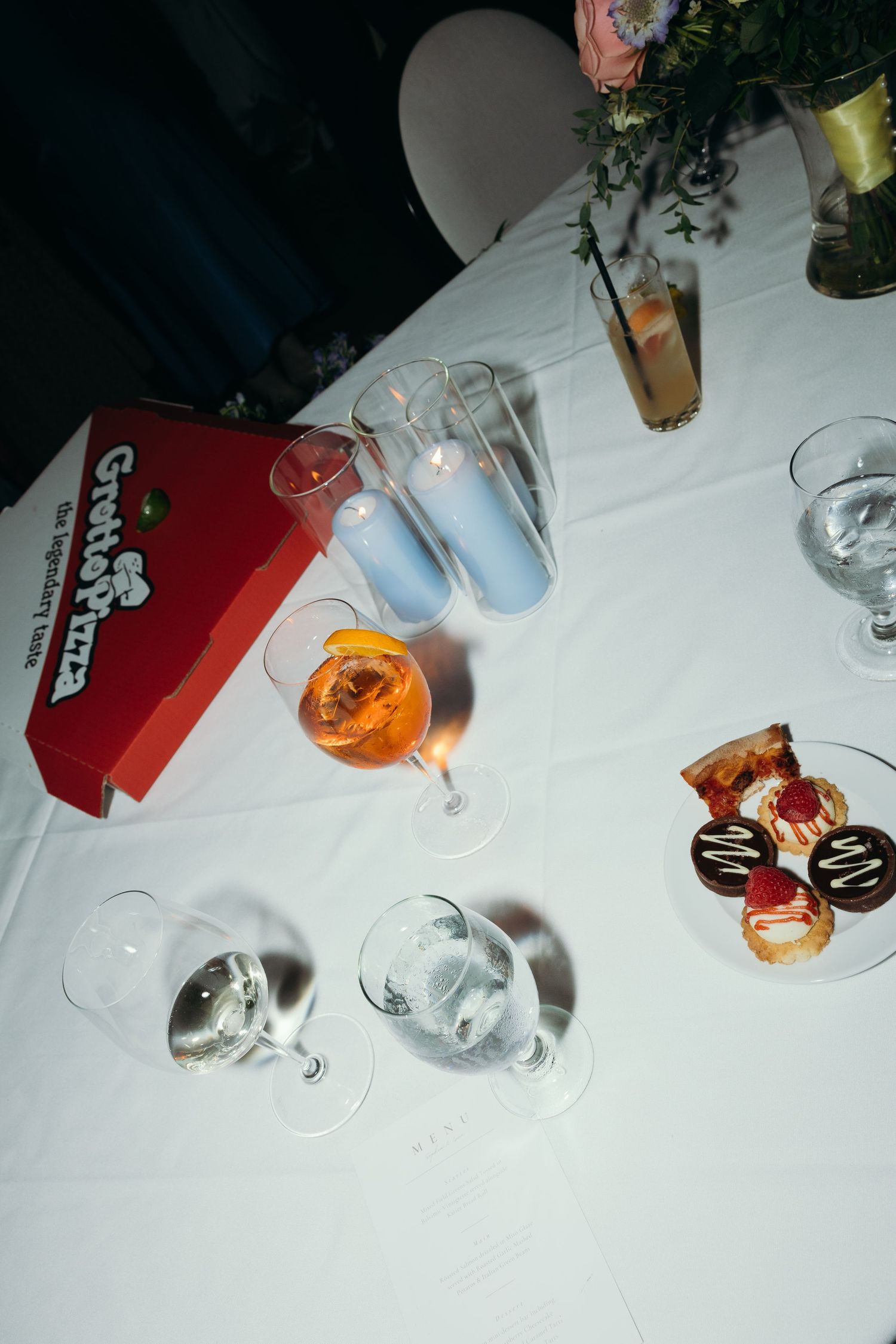 Table setting with cocktail glasses and drinks on white tablecloth at reception.