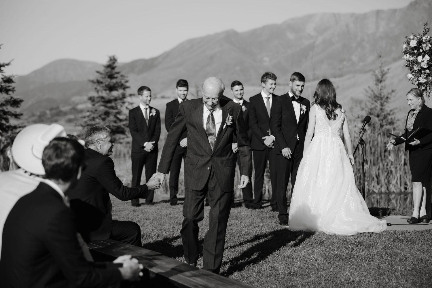 Wedding ceremony procession with mountain peaks and evergreen trees in background.