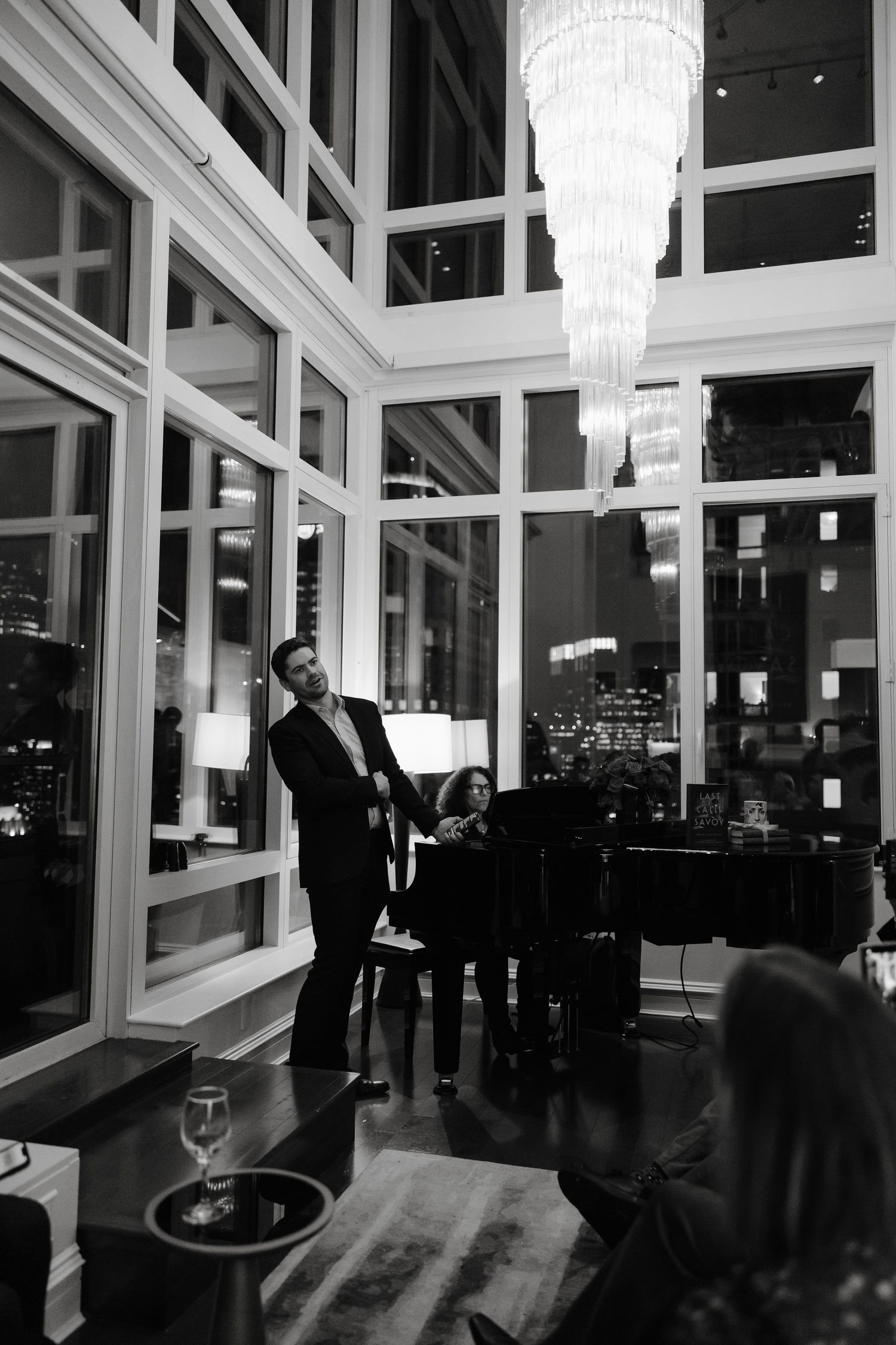 Elegant event space with floor-to-ceiling windows and crystal chandeliers illuminating silhouettes of guests at night for Brisa Carlton