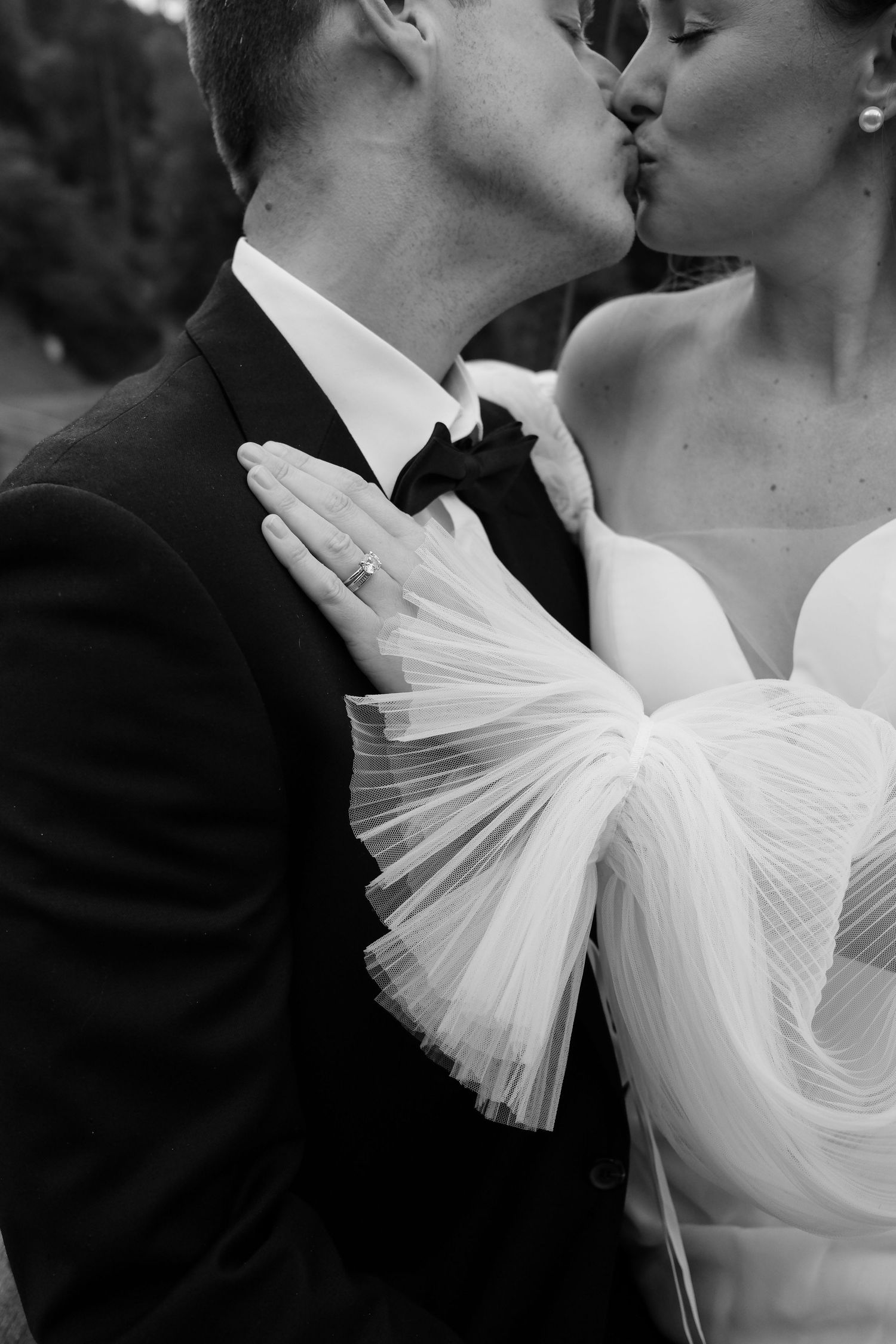 Black and white close-up of romantic wedding moment with dramatic tulle dress detail.