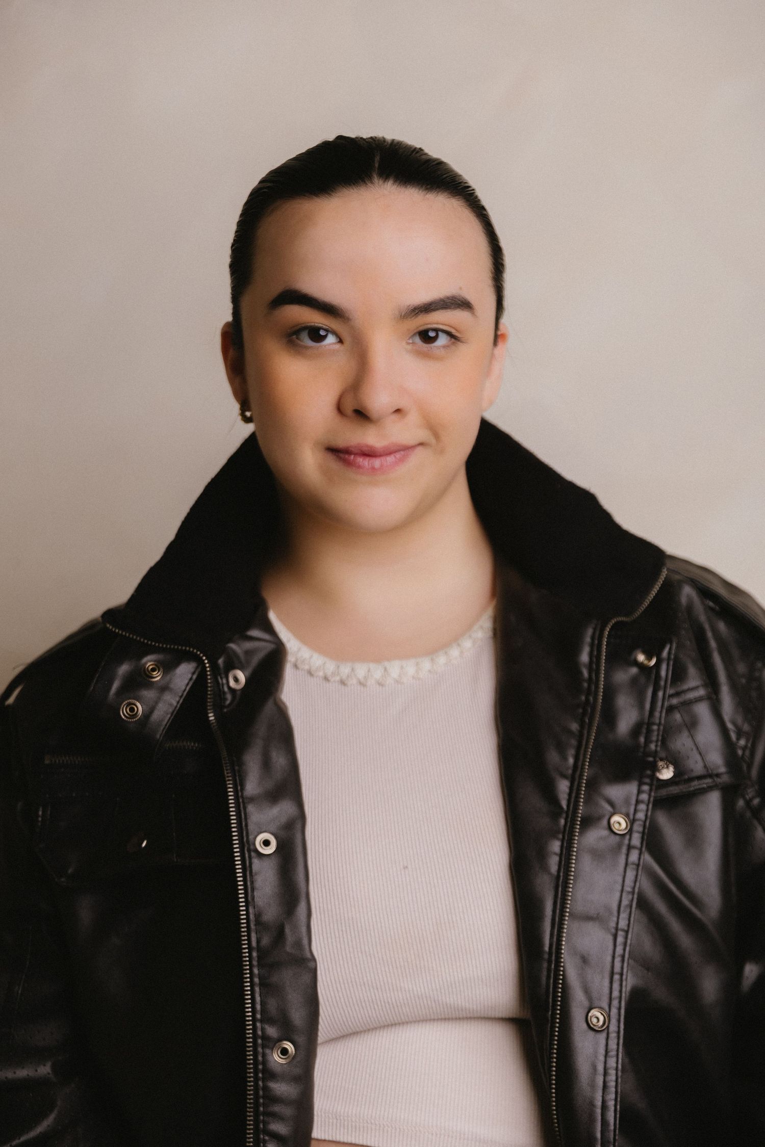 Portrait of someone in a black leather jacket and light colored top against a neutral background.