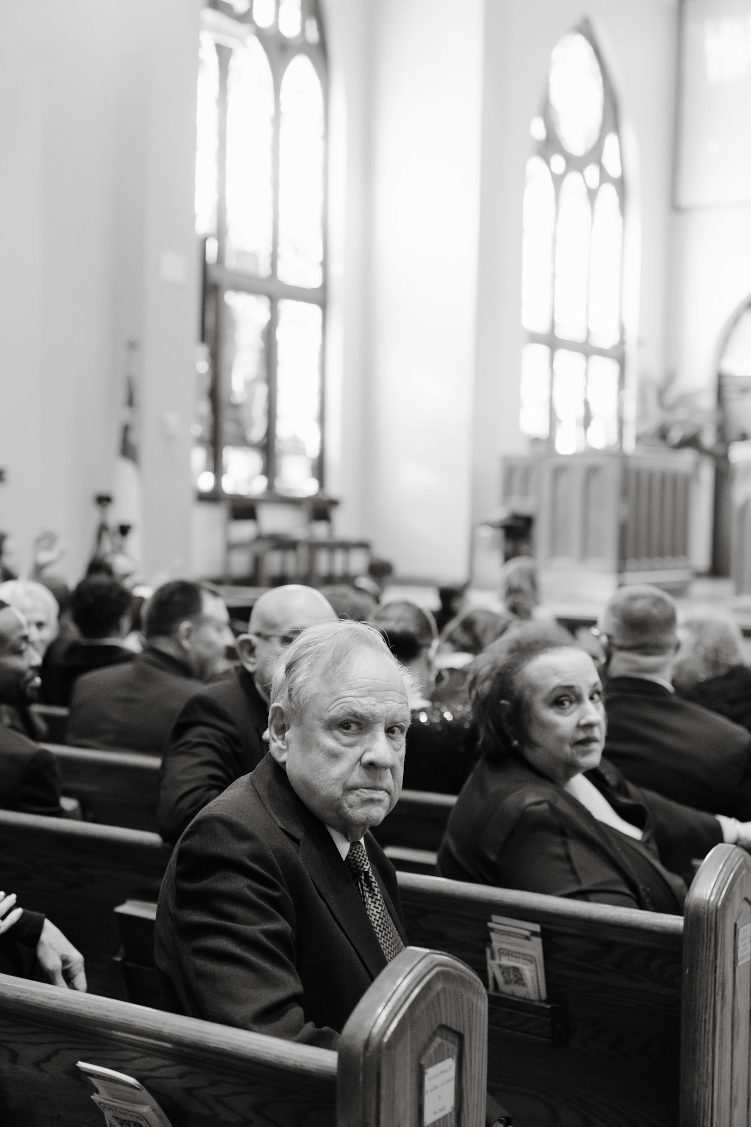Black and white photo of people sitting in wooden church pews during a service.