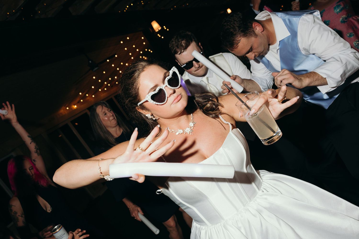 Bride in white dress and heart-shaped sunglasses dancing at wedding reception party.