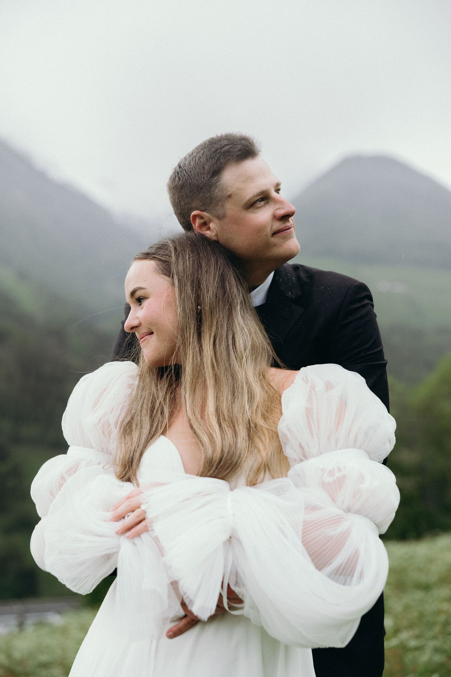 Romantic couple embracing against misty mountain backdrop in wedding attire.