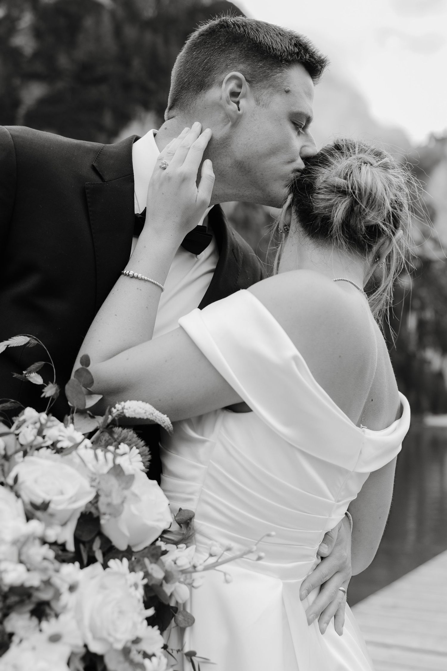 Black and white intimate portrait of newlyweds sharing a tender moment with a floral bouquet.