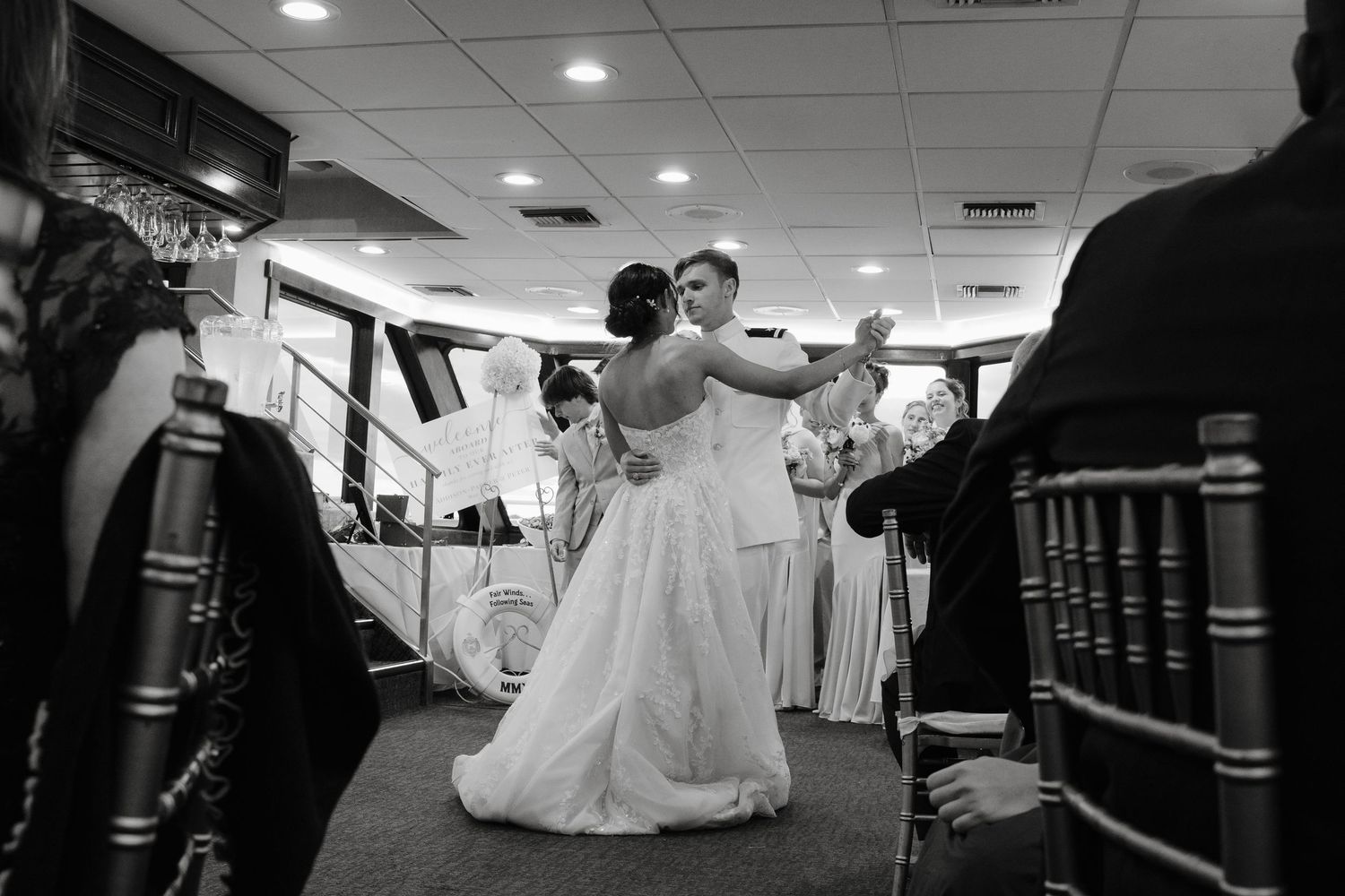 Black and white photo of guests dancing and celebrating at an indoor reception venue.