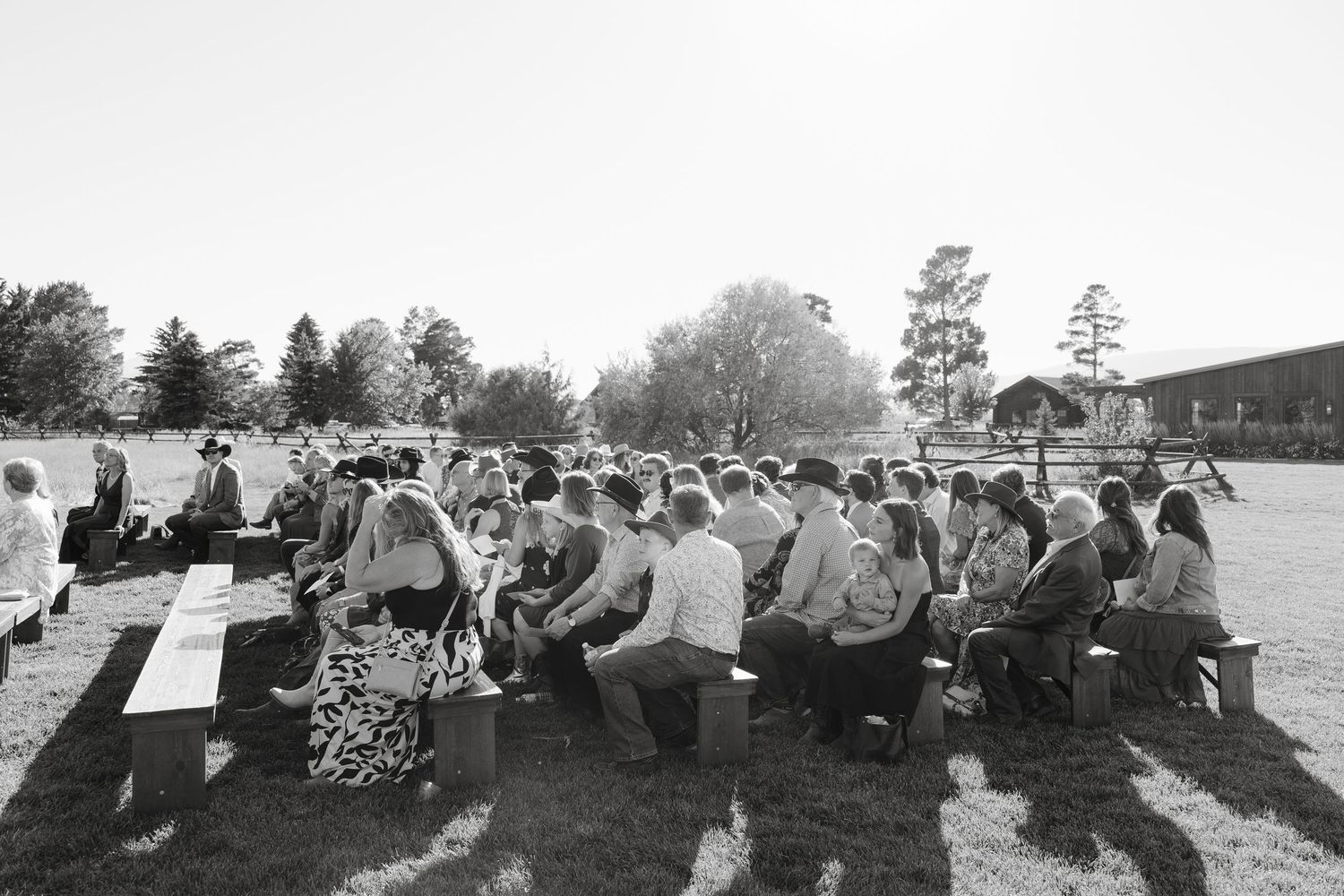 Wedding guests seated outdoors for ceremony in black and white photography.