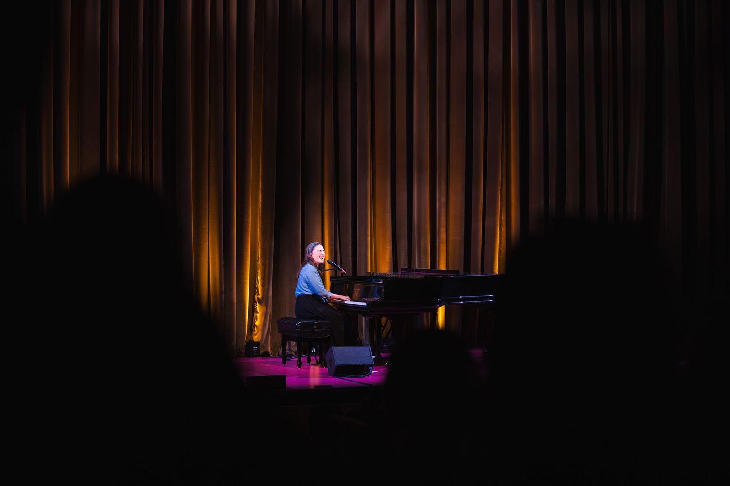 A piano performance on a dimly lit stage with dramatic spotlighting and dark curtains in the background.