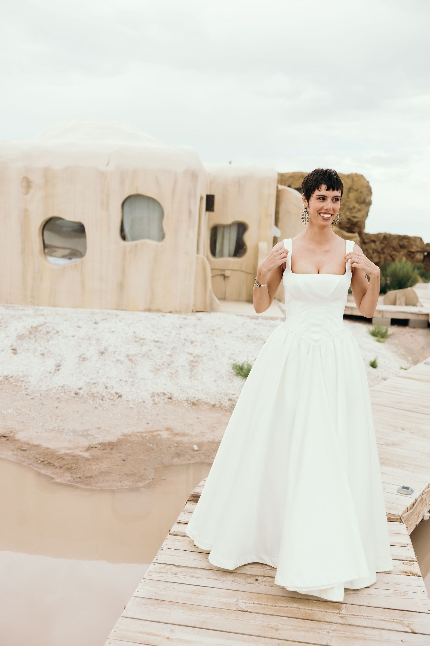 A flowing white wedding dress photographed in a desert-like setting with adobe buildings in the background.