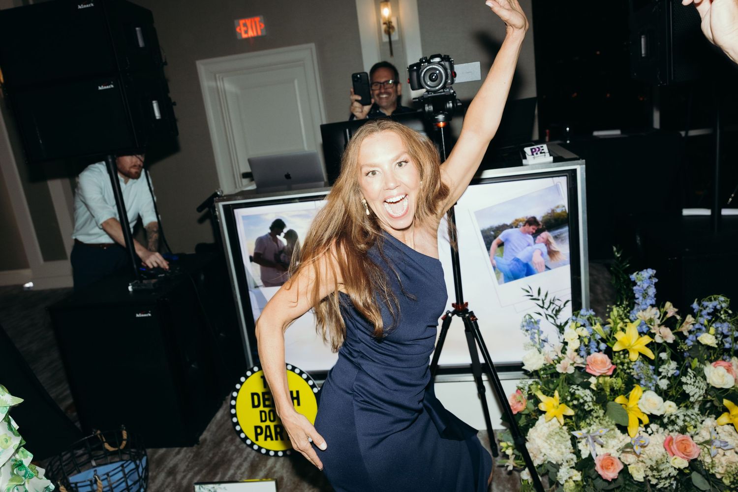 Wedding guests dancing and celebrating on a dimly lit dance floor with floral decorations.